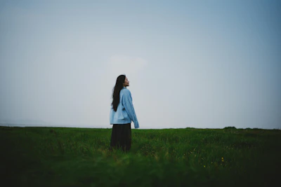 A woman stands in a grassy field looking up