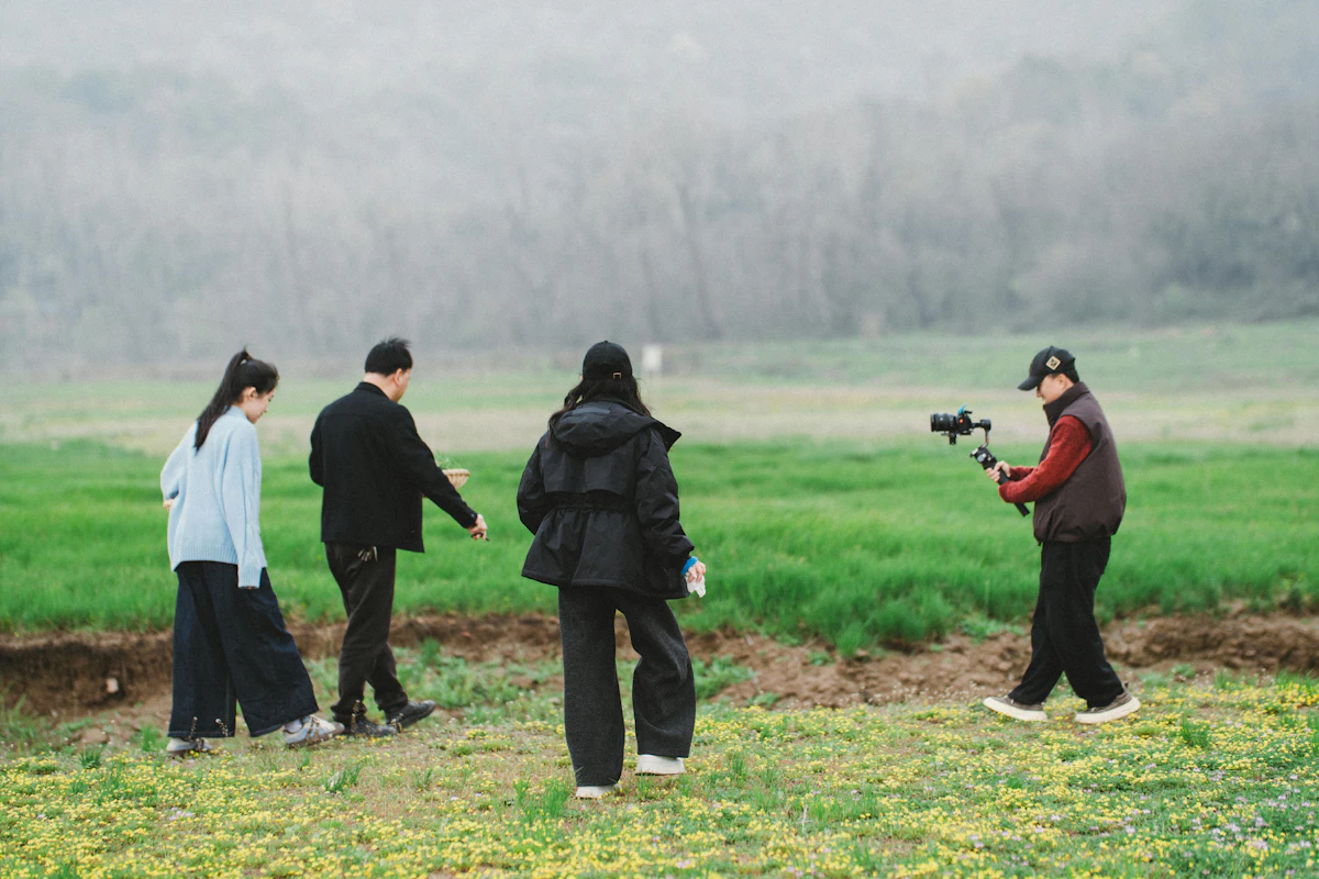 People walking through a grassy field while a crew member records