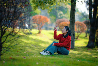 Young woman sitting in a park reaching for a leaf.