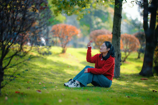 Young woman sitting in a park reaching for a leaf.