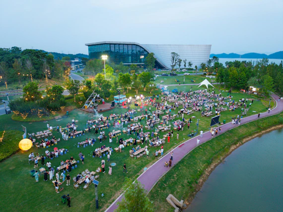 People gather on grass near a modern building at dusk.