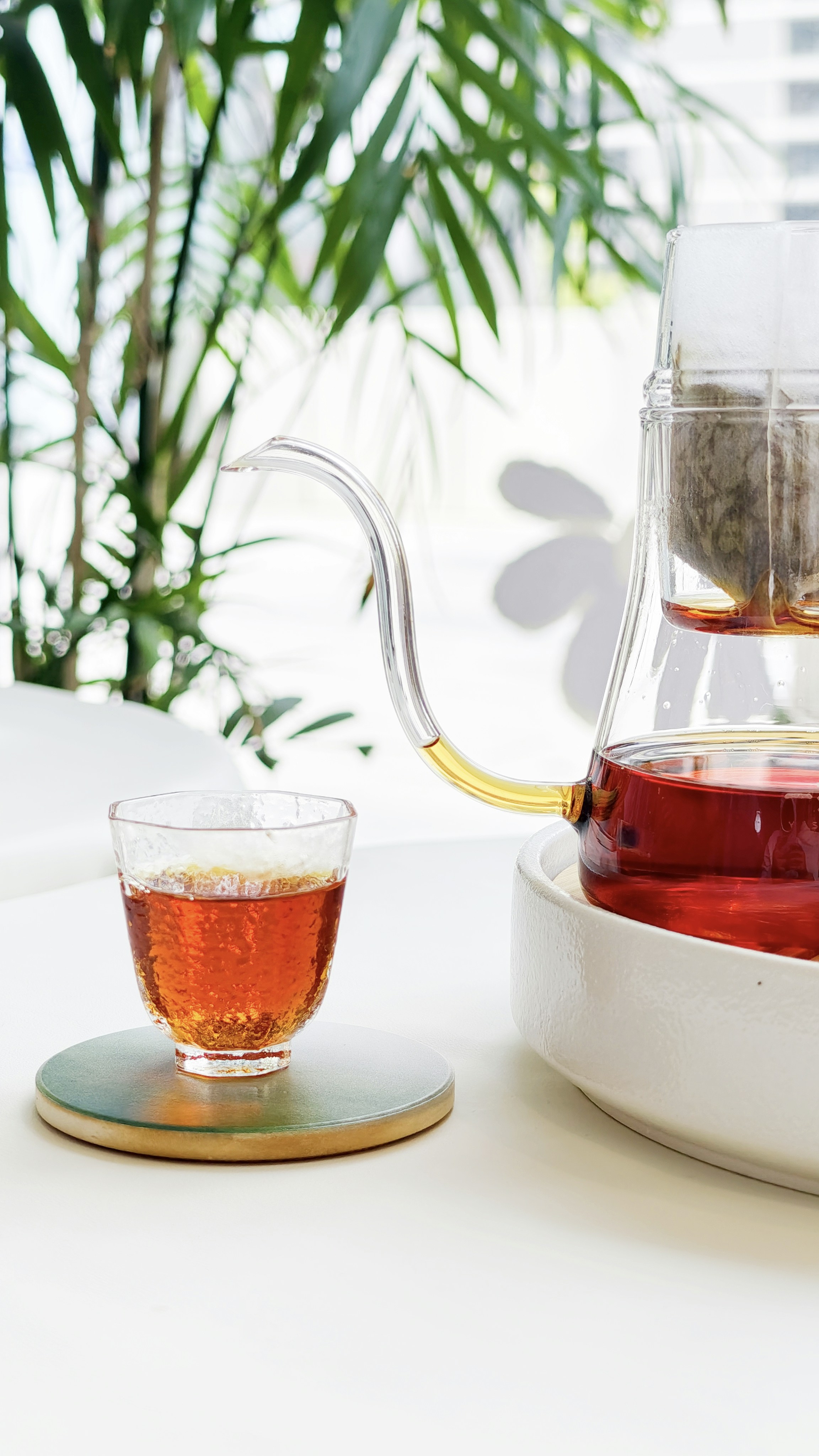 A glass of amber tea next to a tea maker.
