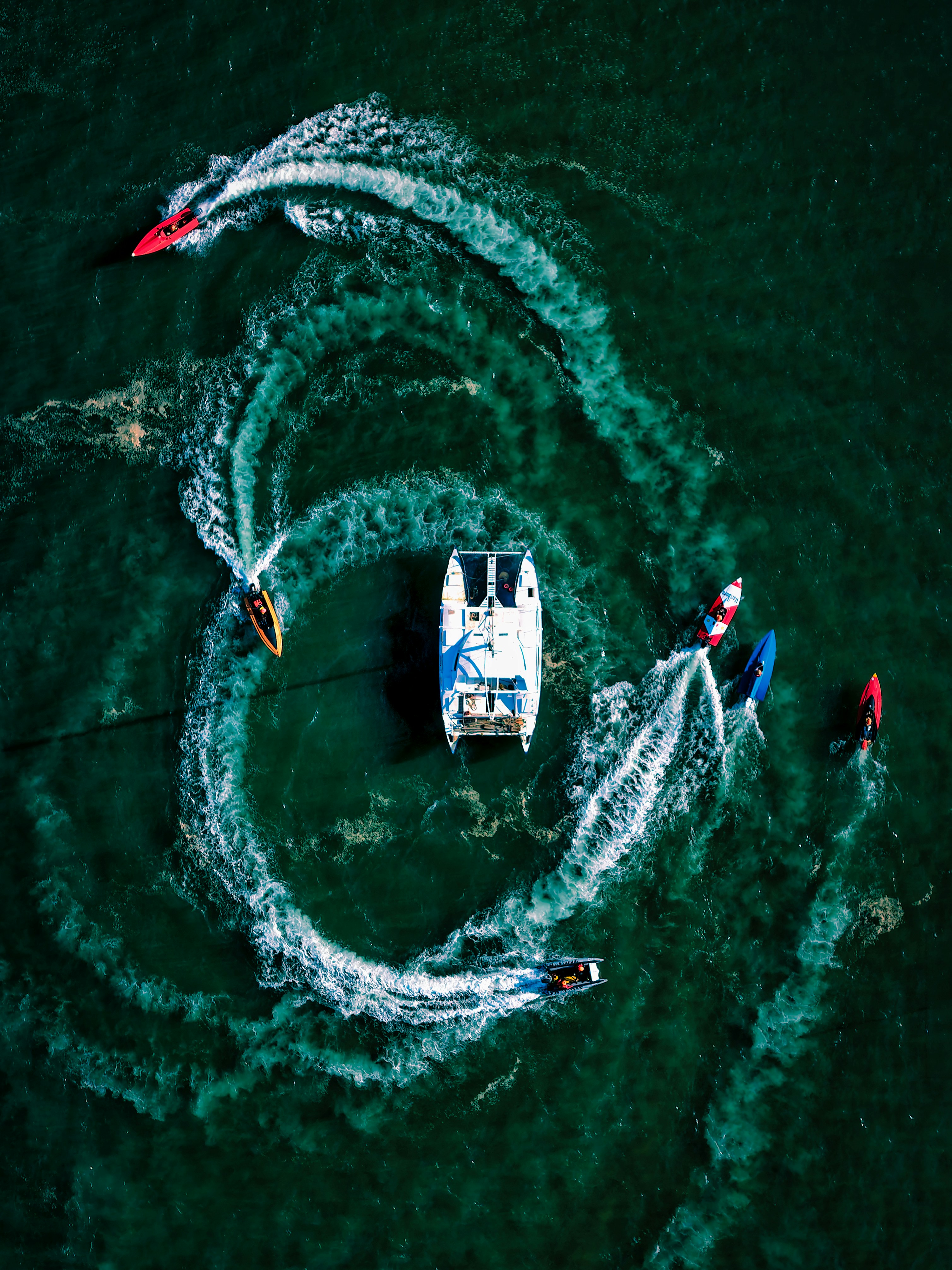 Sailboat and jet skis create swirling patterns on water