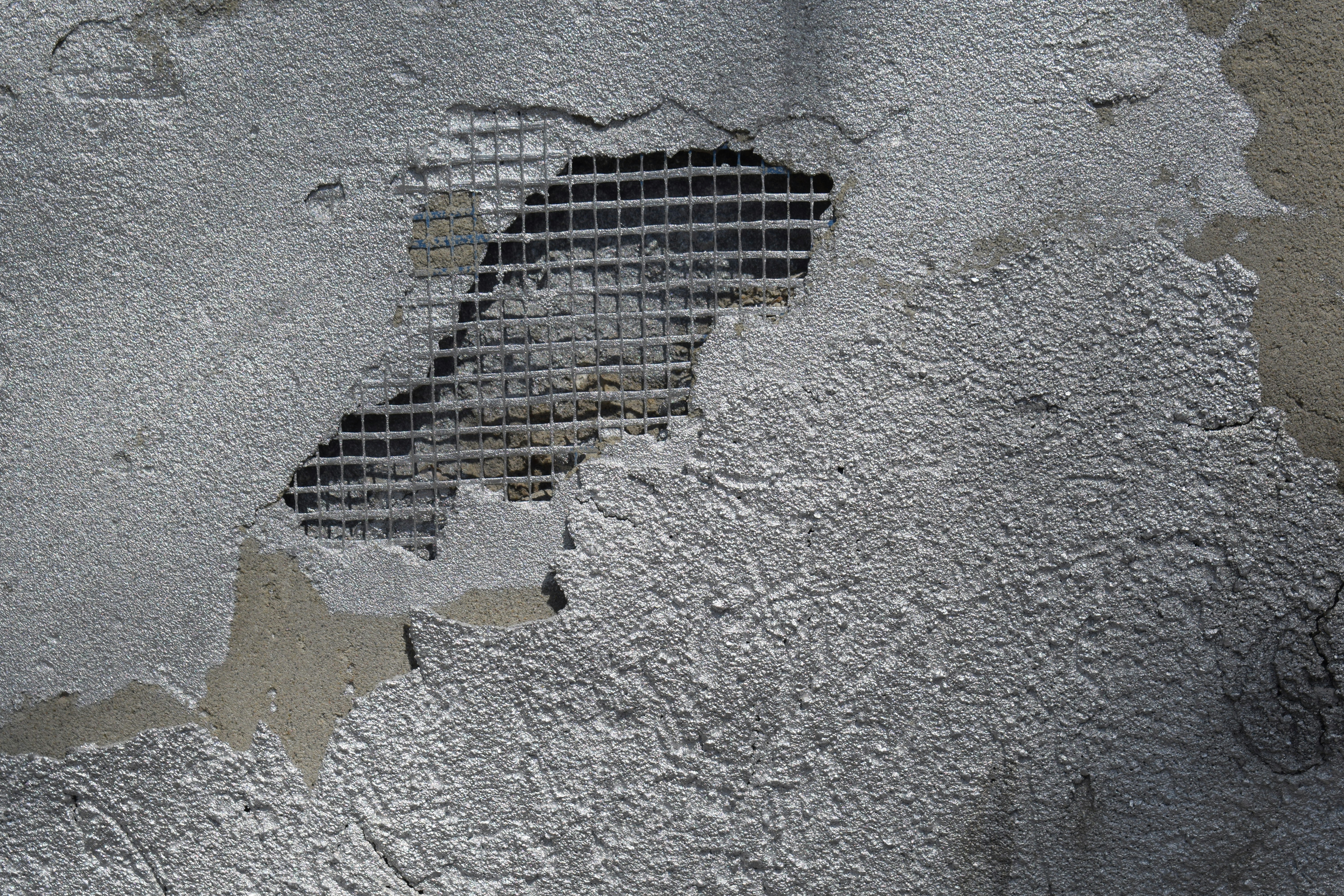 Damaged concrete wall with exposed metal mesh