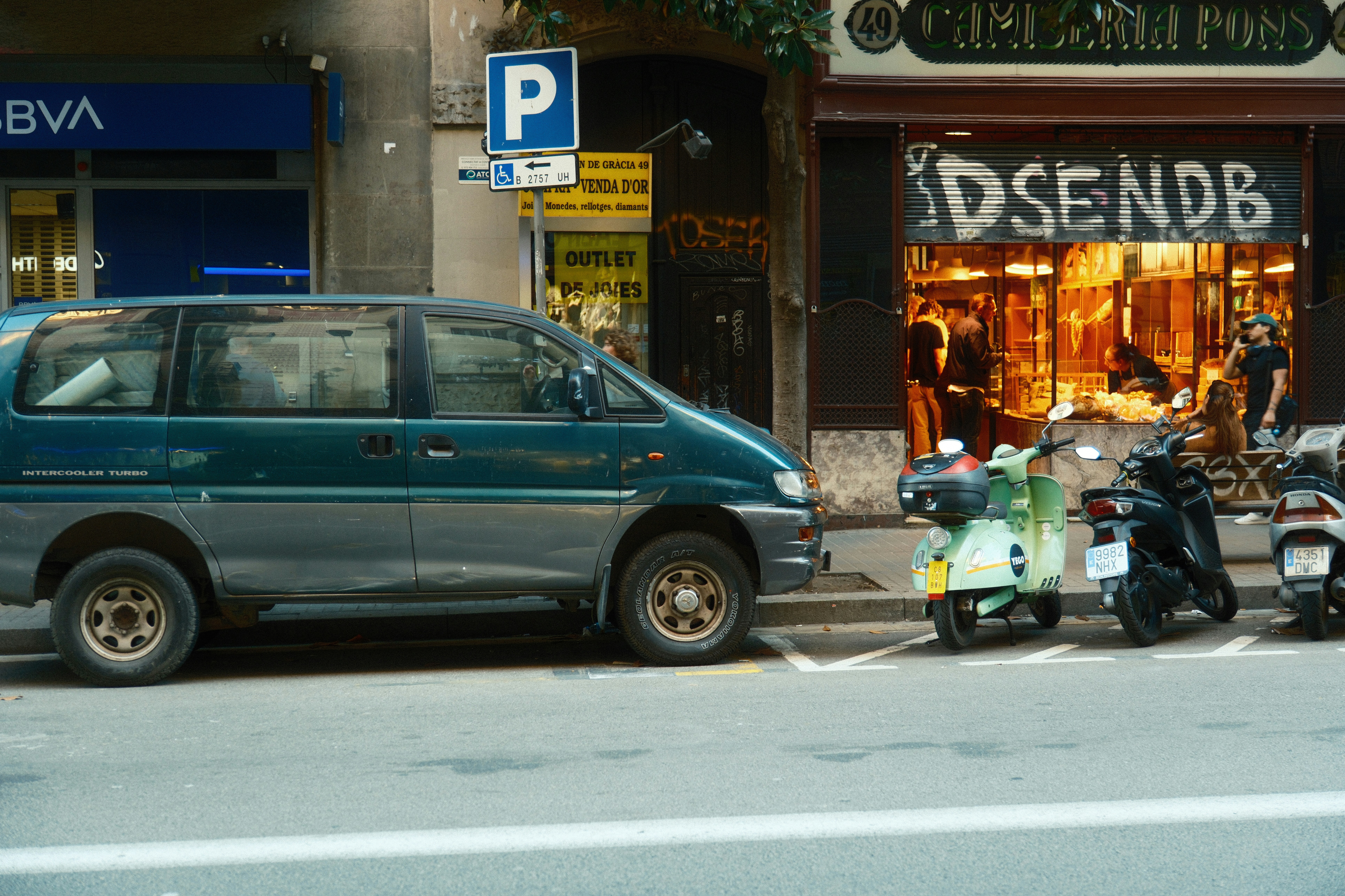 A green van parked next to scooters on street.
