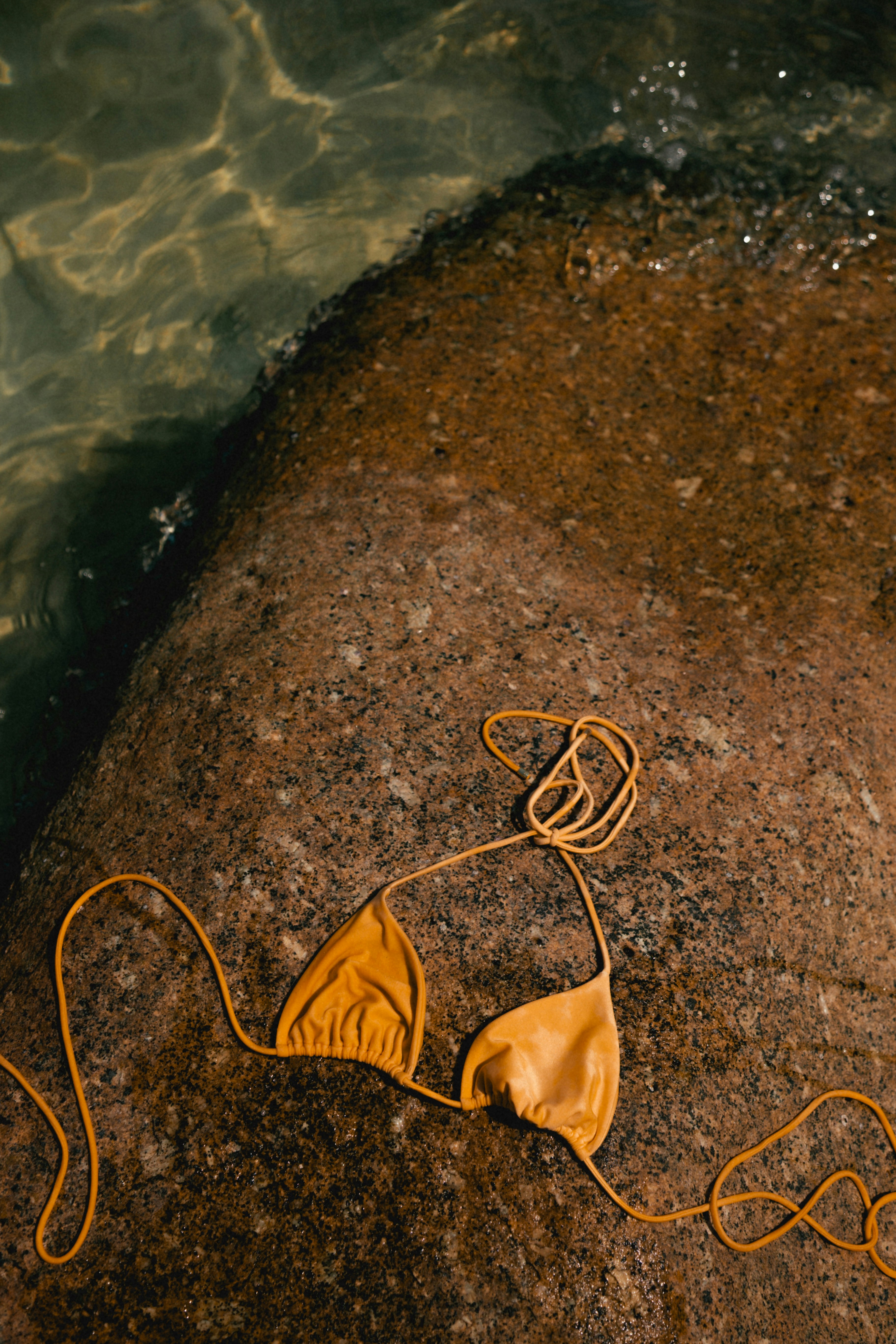 Yellow bikini top resting on a wet rock near water