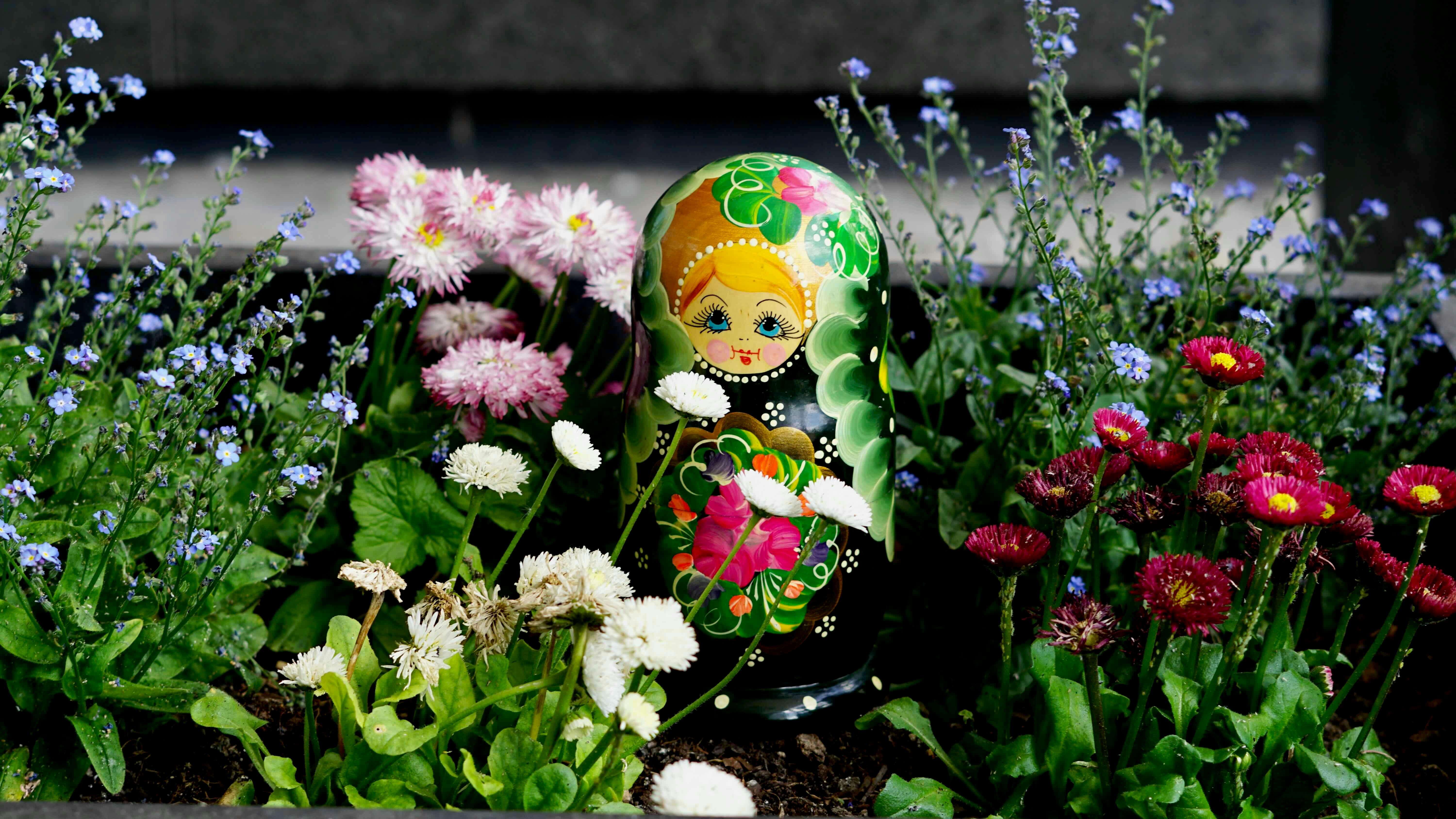 色とりどりの庭の花々の間に寄り添うマトリョーシカ人形。