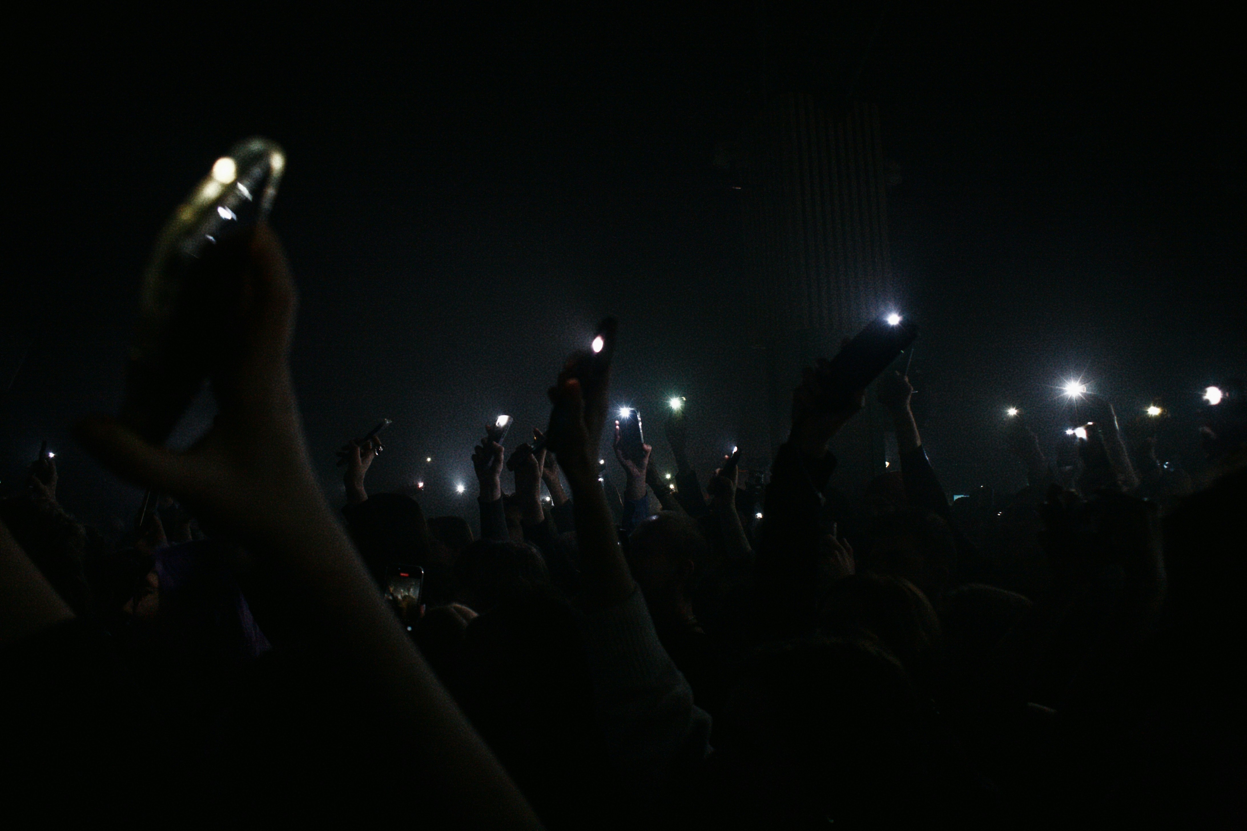 Hands holding up phone lights at a concert.