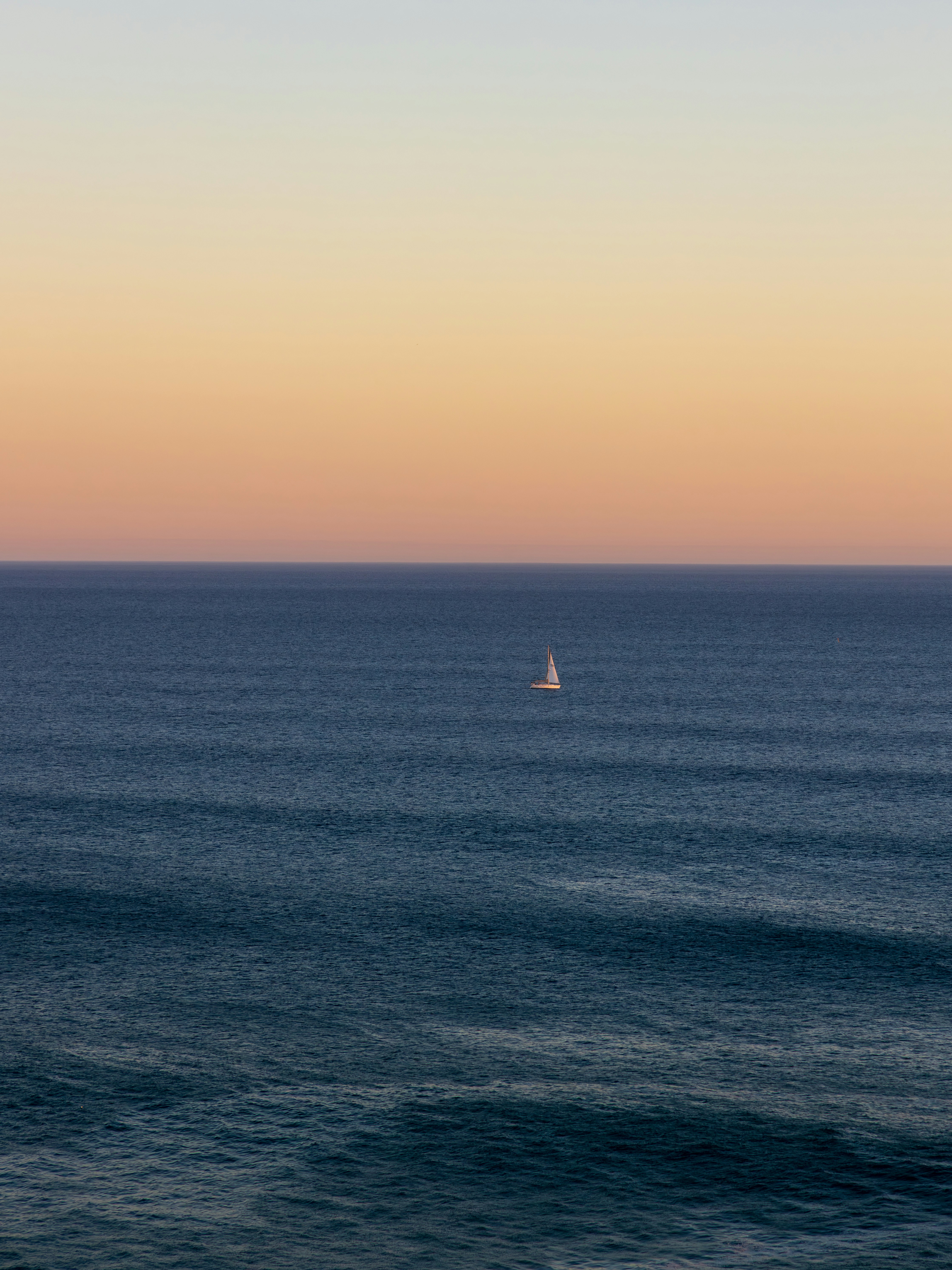 A lone sailboat on the vast ocean at sunset.