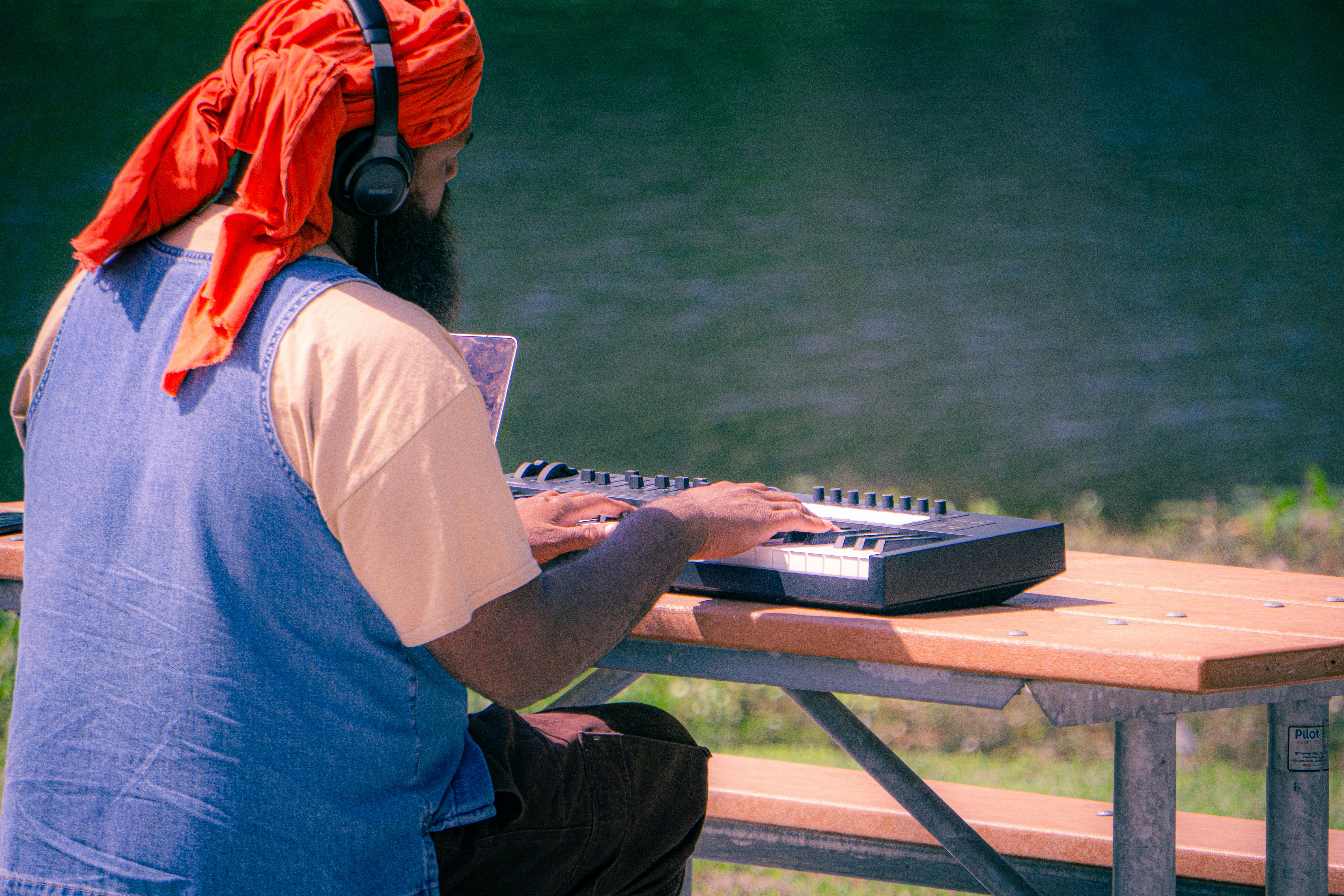 Man with headphones plays keyboard outdoors by water