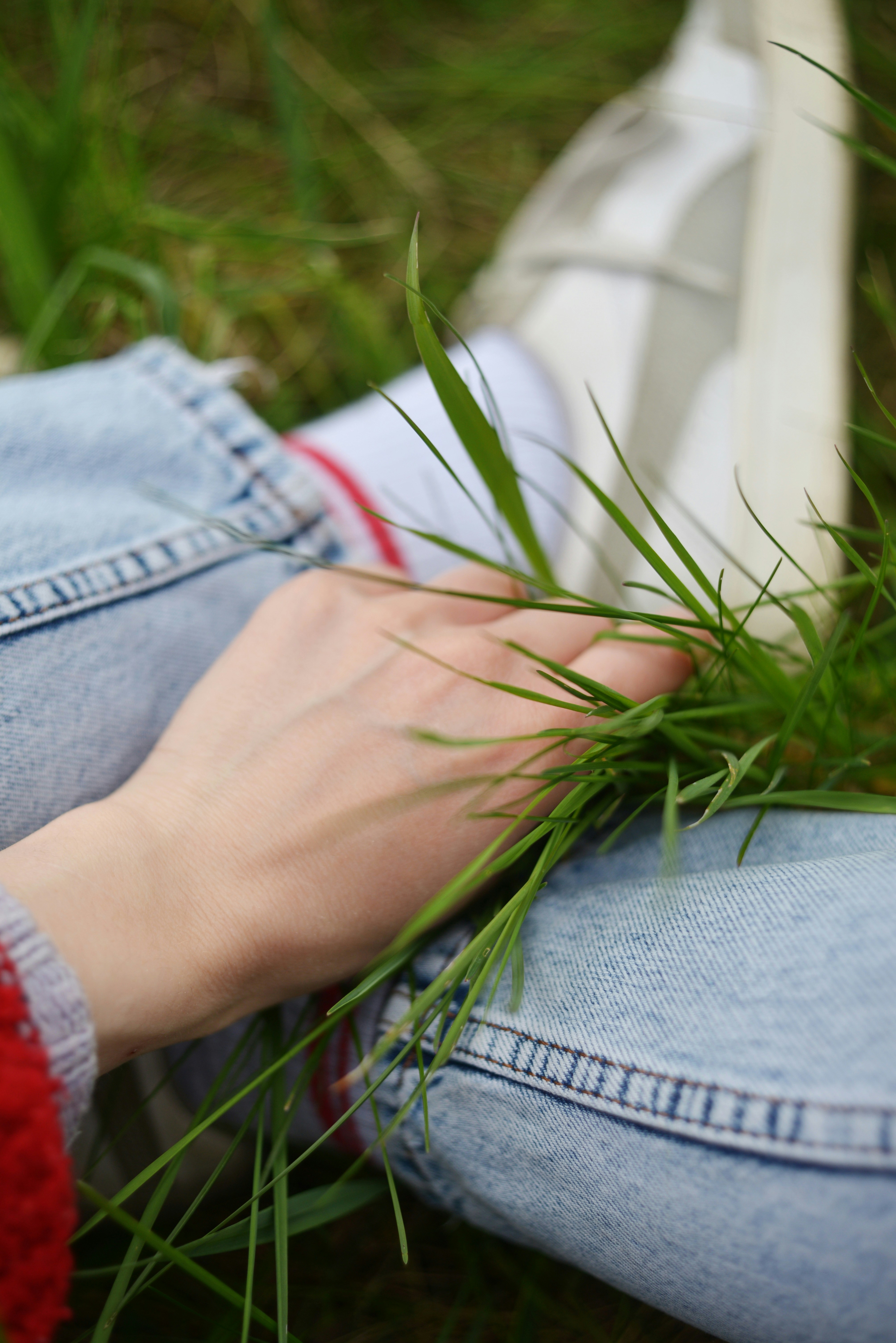 ジーンズ姿で草の上に手を置く人の手