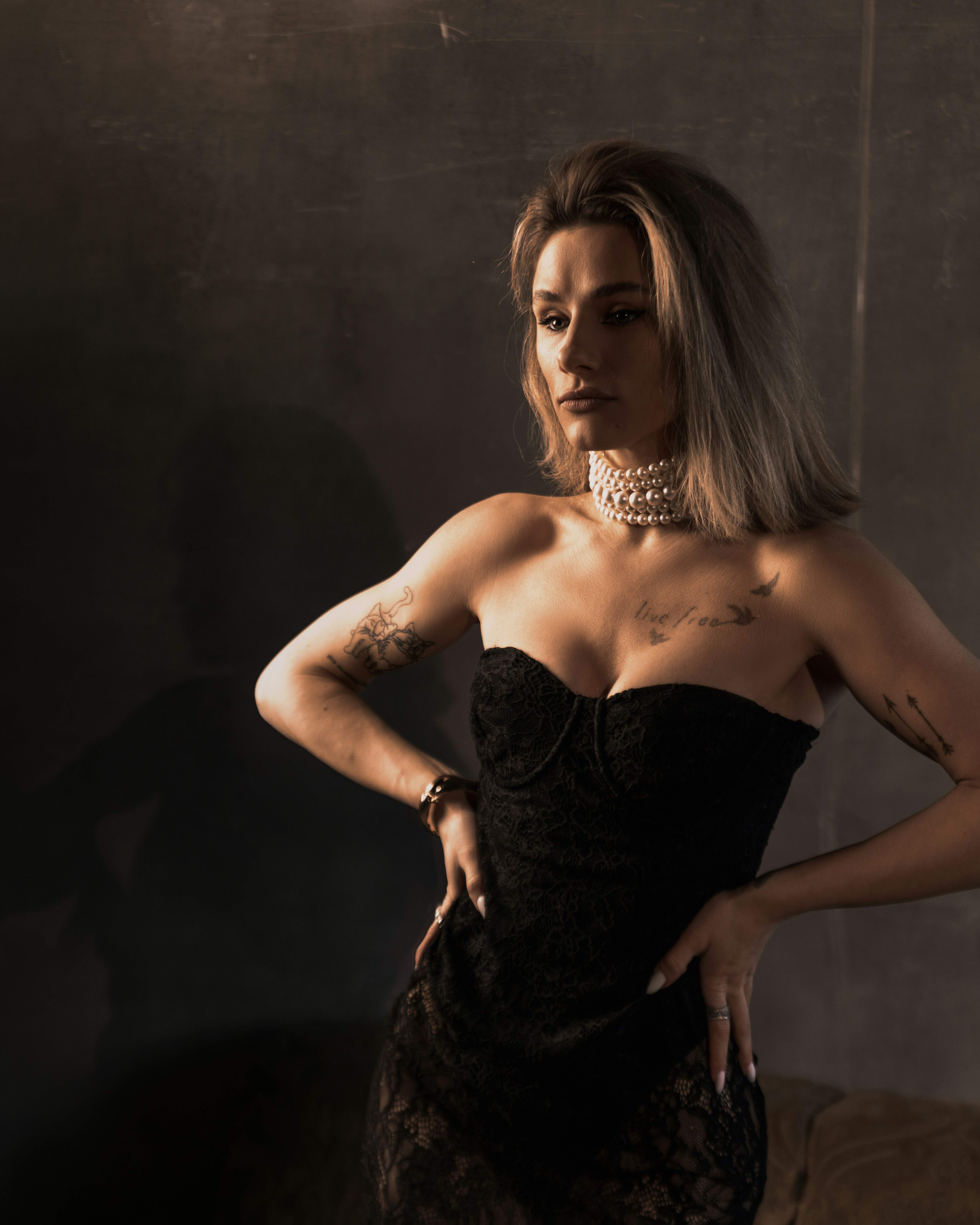 A woman in a black lace dress and pearl necklace.