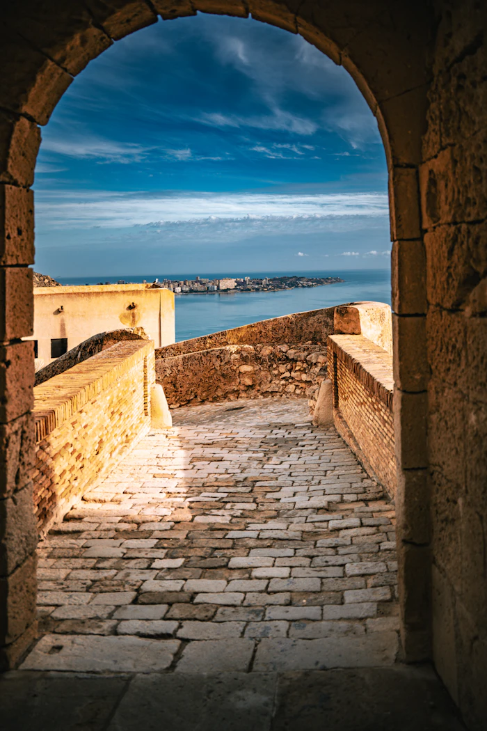 Sentiero in pietra che passa sotto un arco e scende verso il paese sul mare