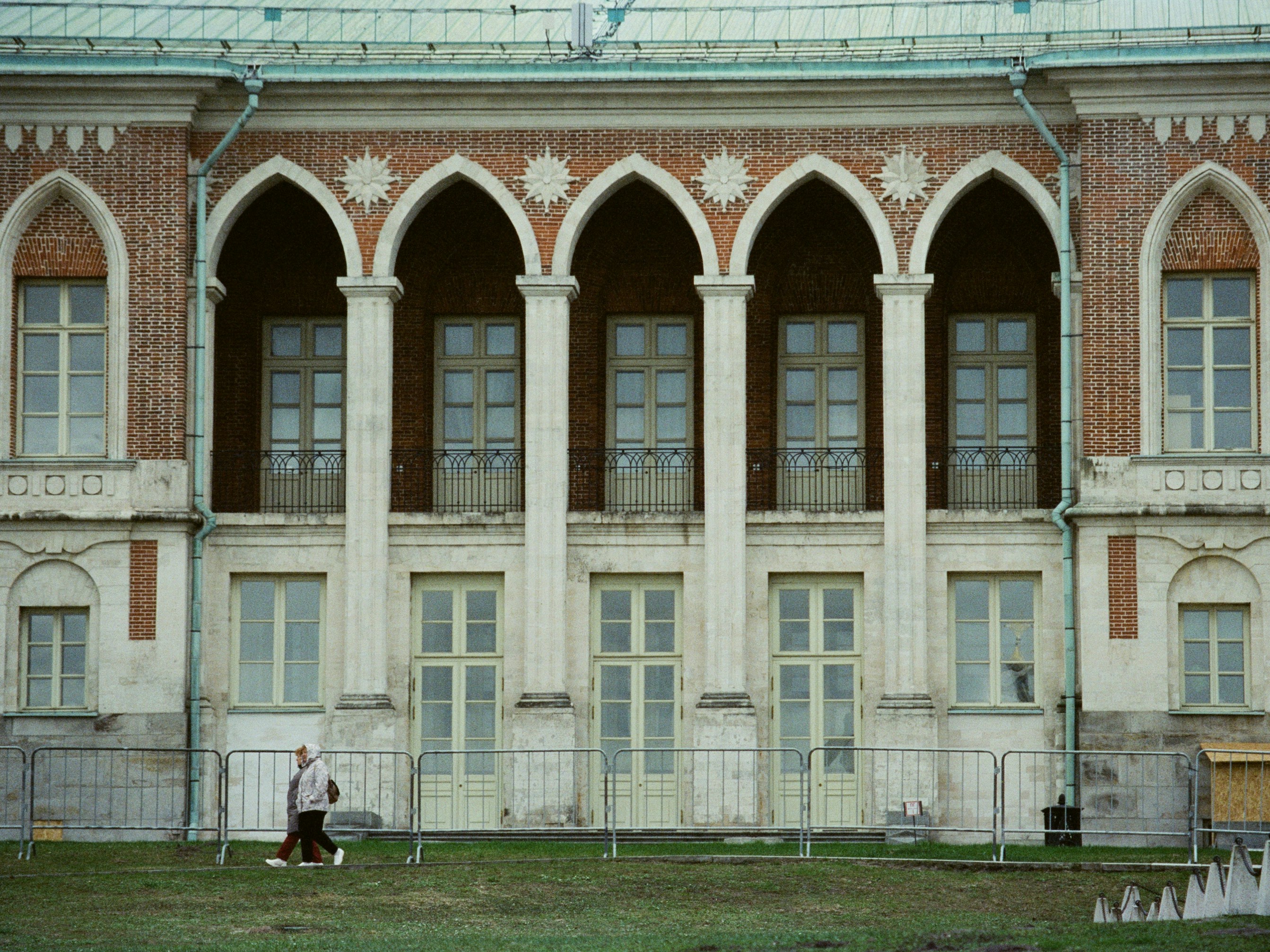 A person walks past a grand building with arched windows.
