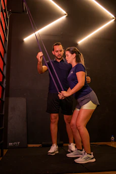 Trainer assisting woman with resistance band exercise.
