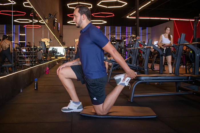 A man stretching his quad on a mat in the gym