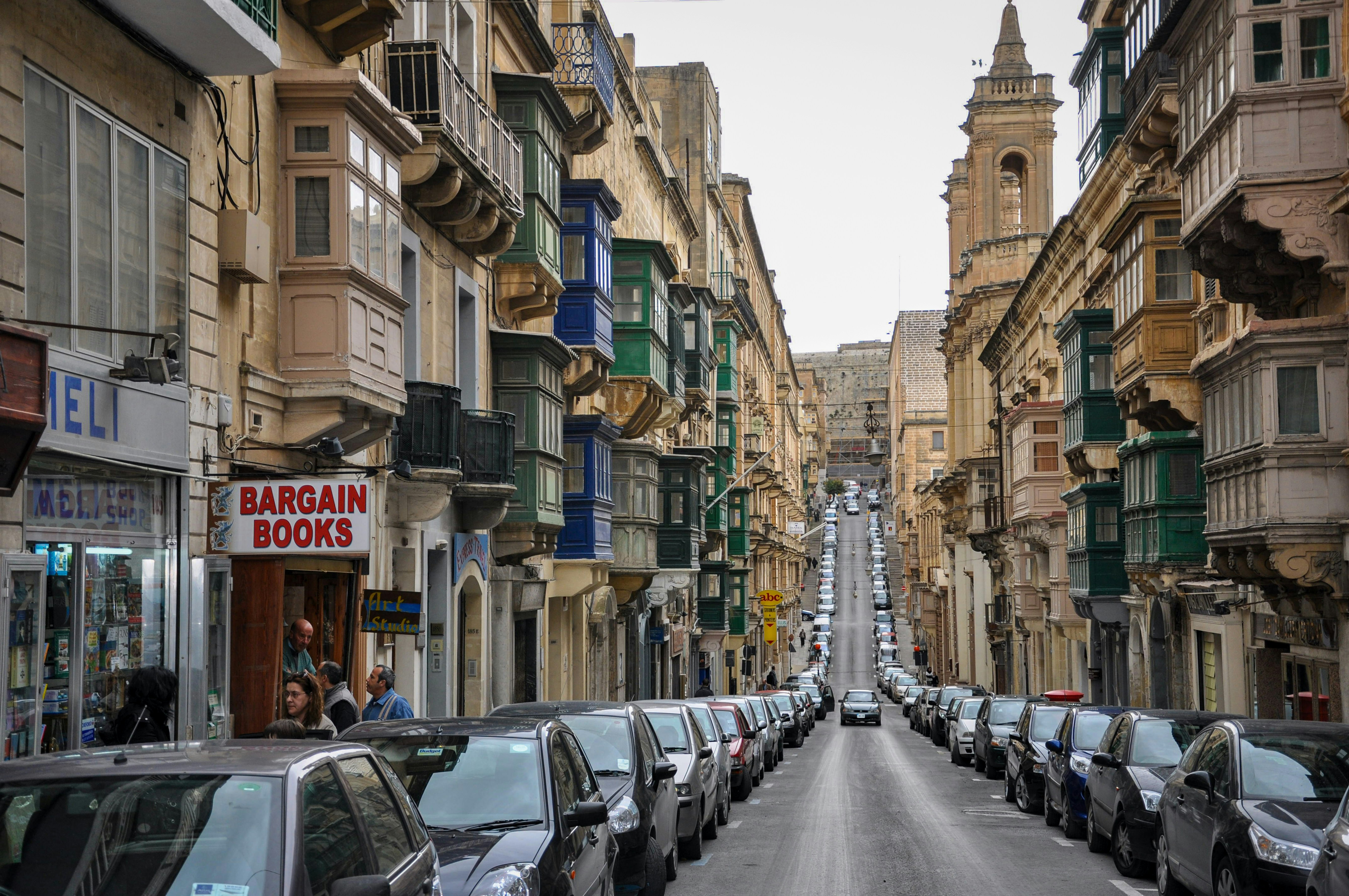 Street lined with cars and traditional maltese balconies.