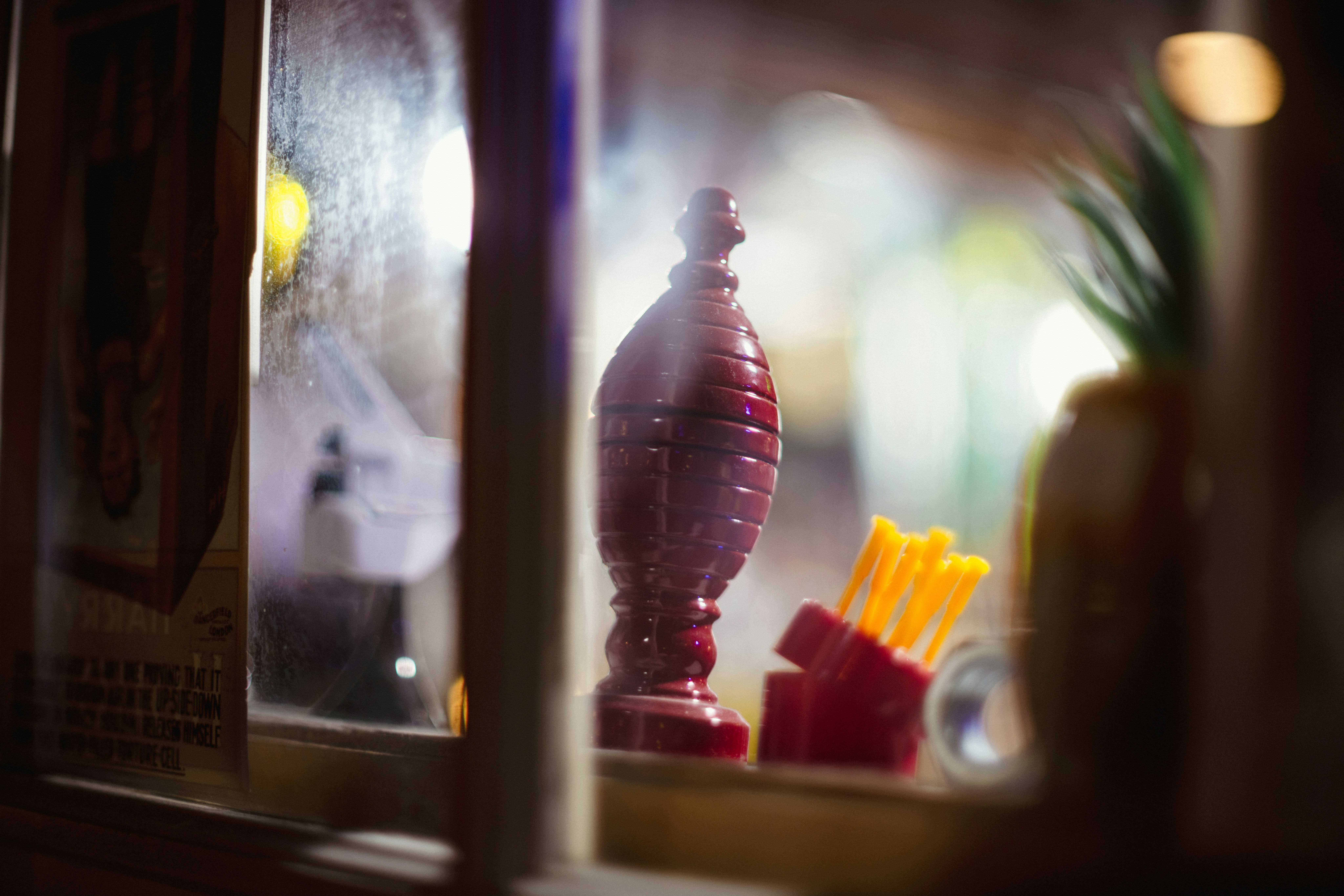 Red glass bottle and yellow sticks behind glass