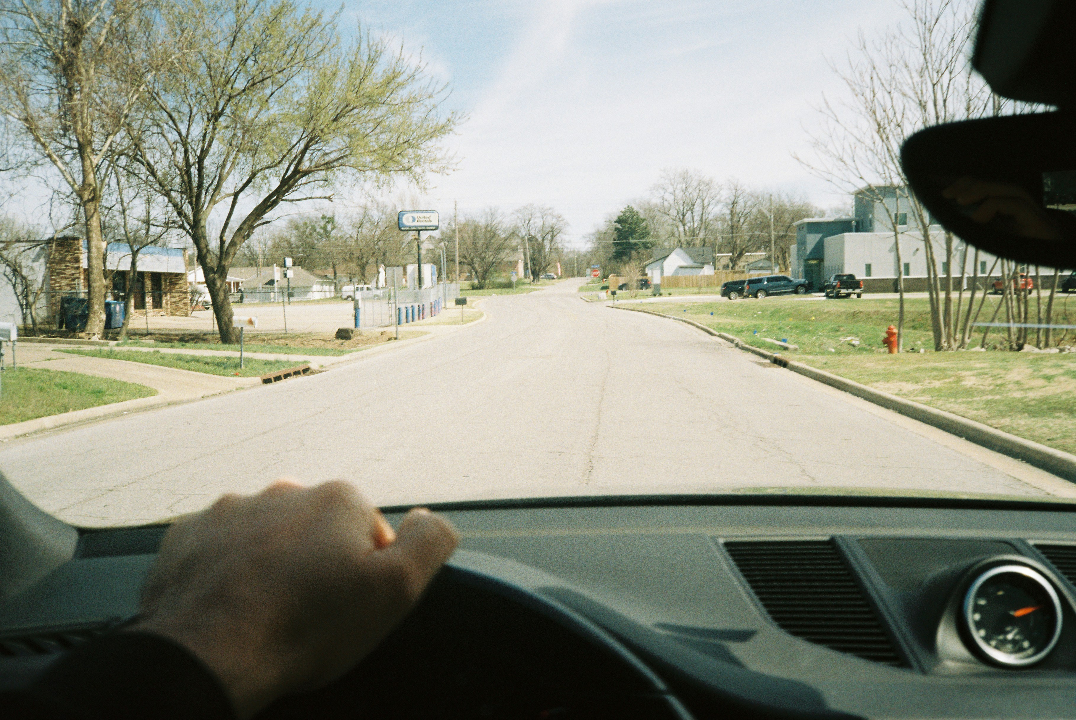 Driver holds a steering wheel while looking down a suburban street.