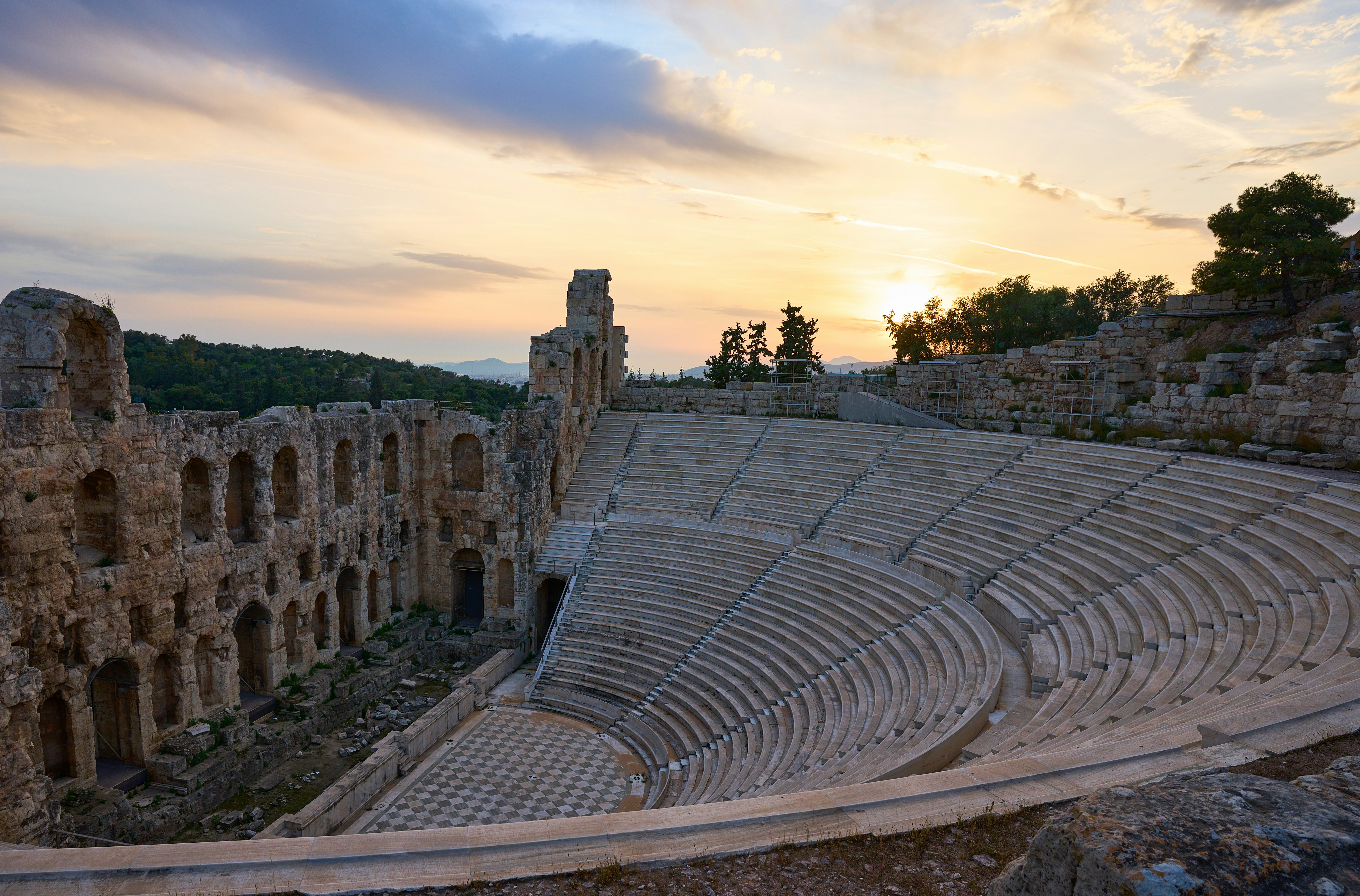 Rovine antiche di anfiteatro al tramonto con un cielo drammatico.