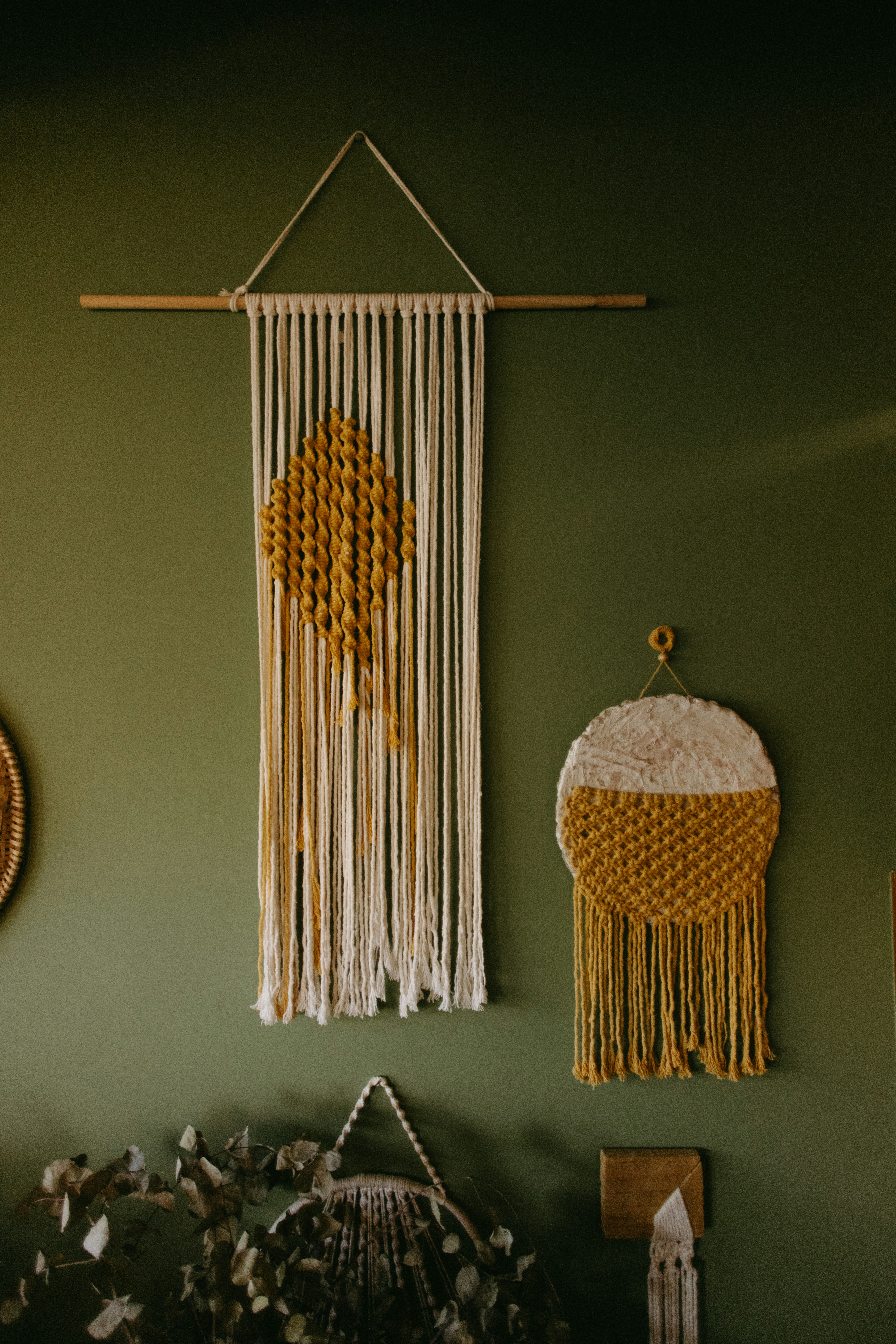 Macrame wall hangings in earthy tones on green wall