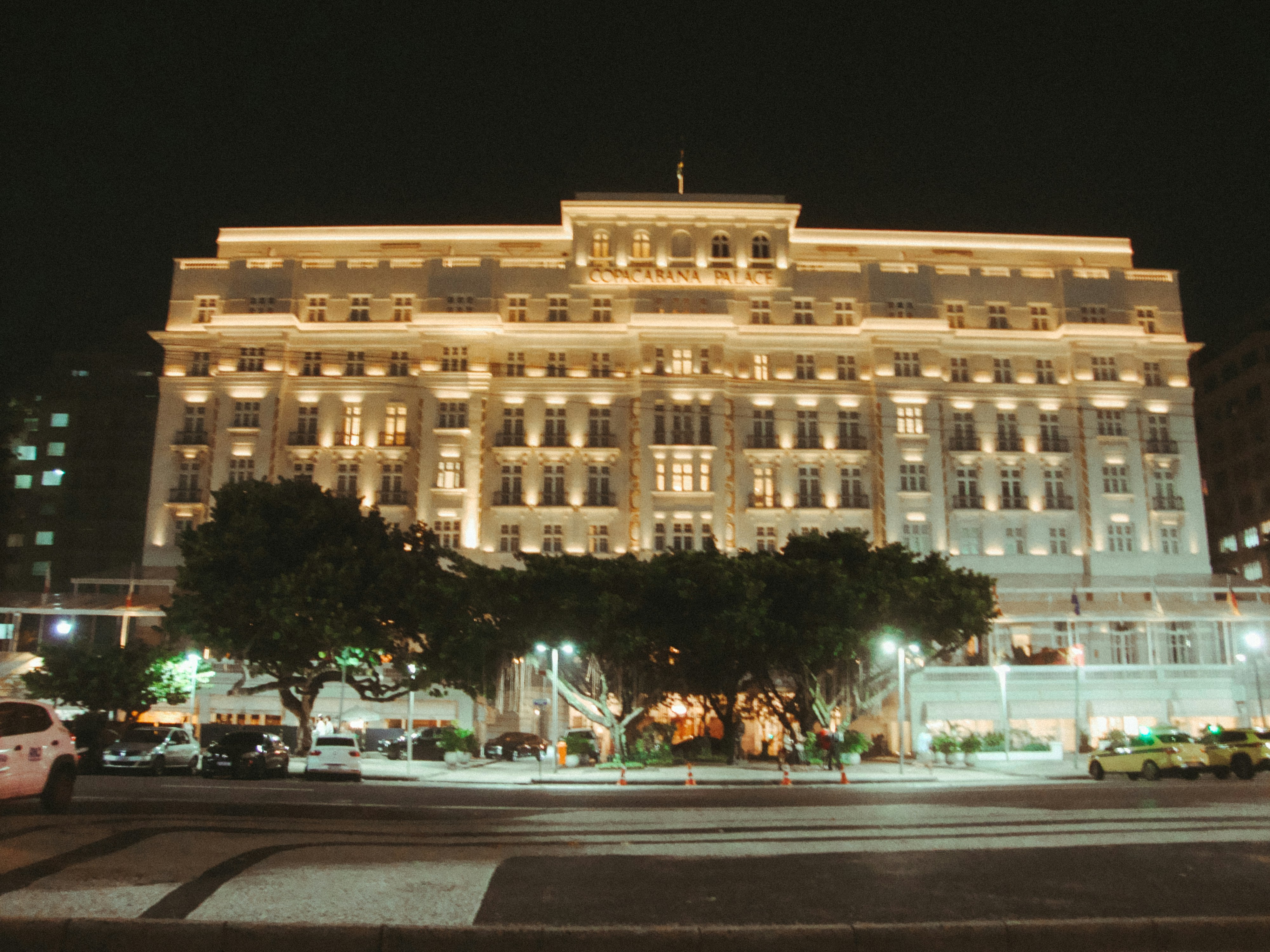 Grand illuminated hotel building at night with trees.