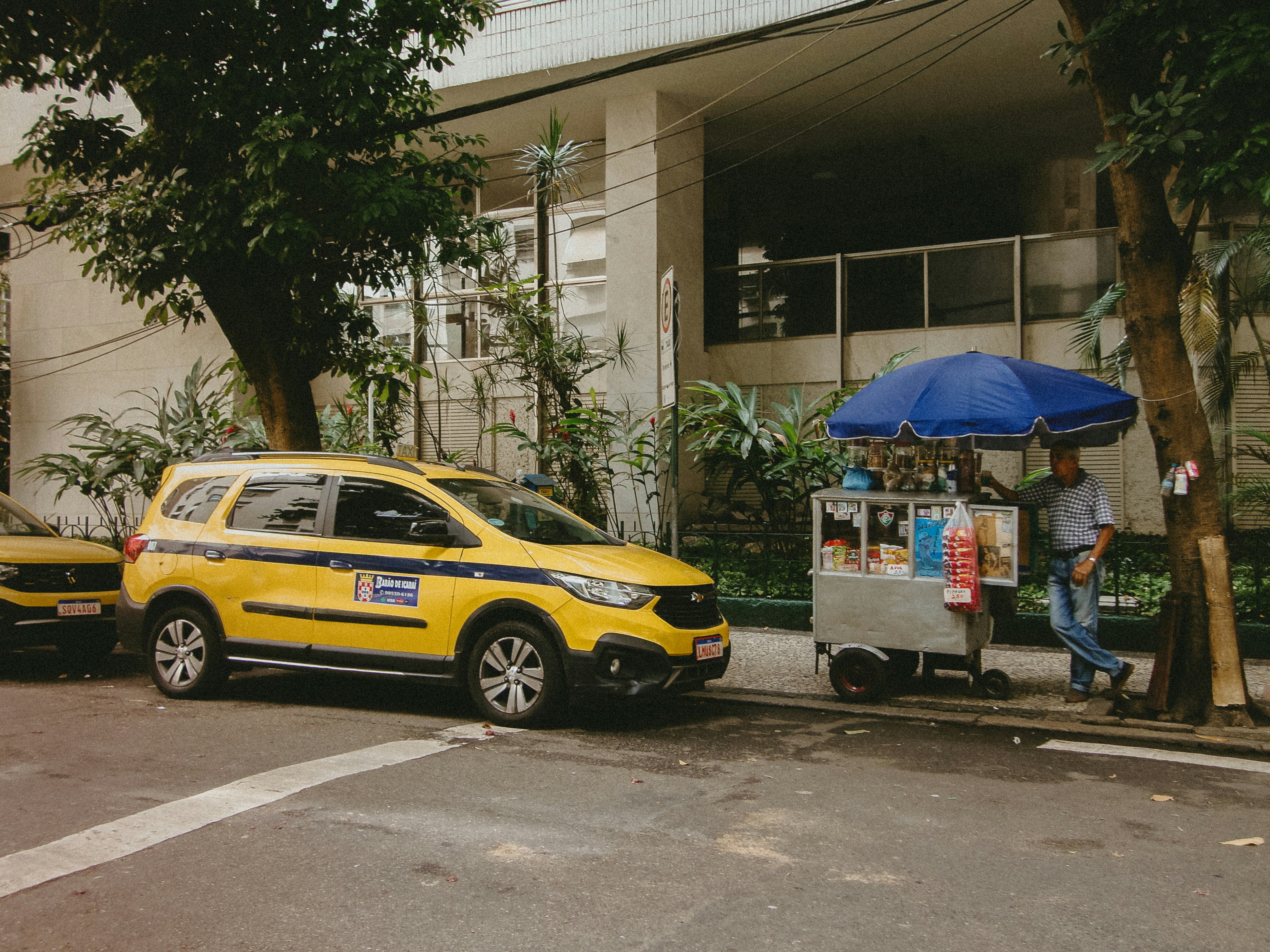 Yellow taxi parked beside a street food cart.