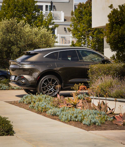 Dark luxury suv parked near modern buildings and plants.