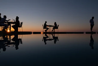 Silhouettes of people dining by the ocean at sunset.