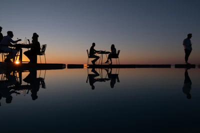 Silhouettes of people dining by the ocean at sunset.