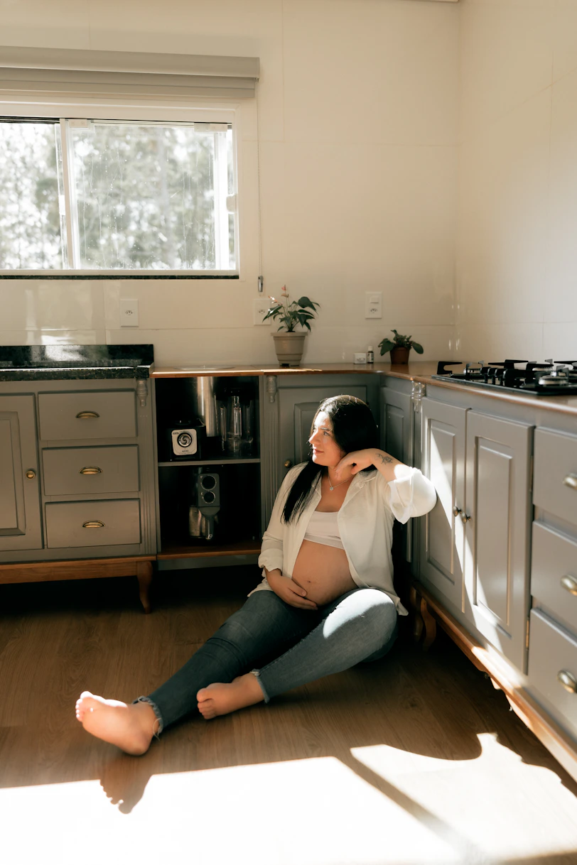 Pregnant woman sitting on the floor in a kitchen.