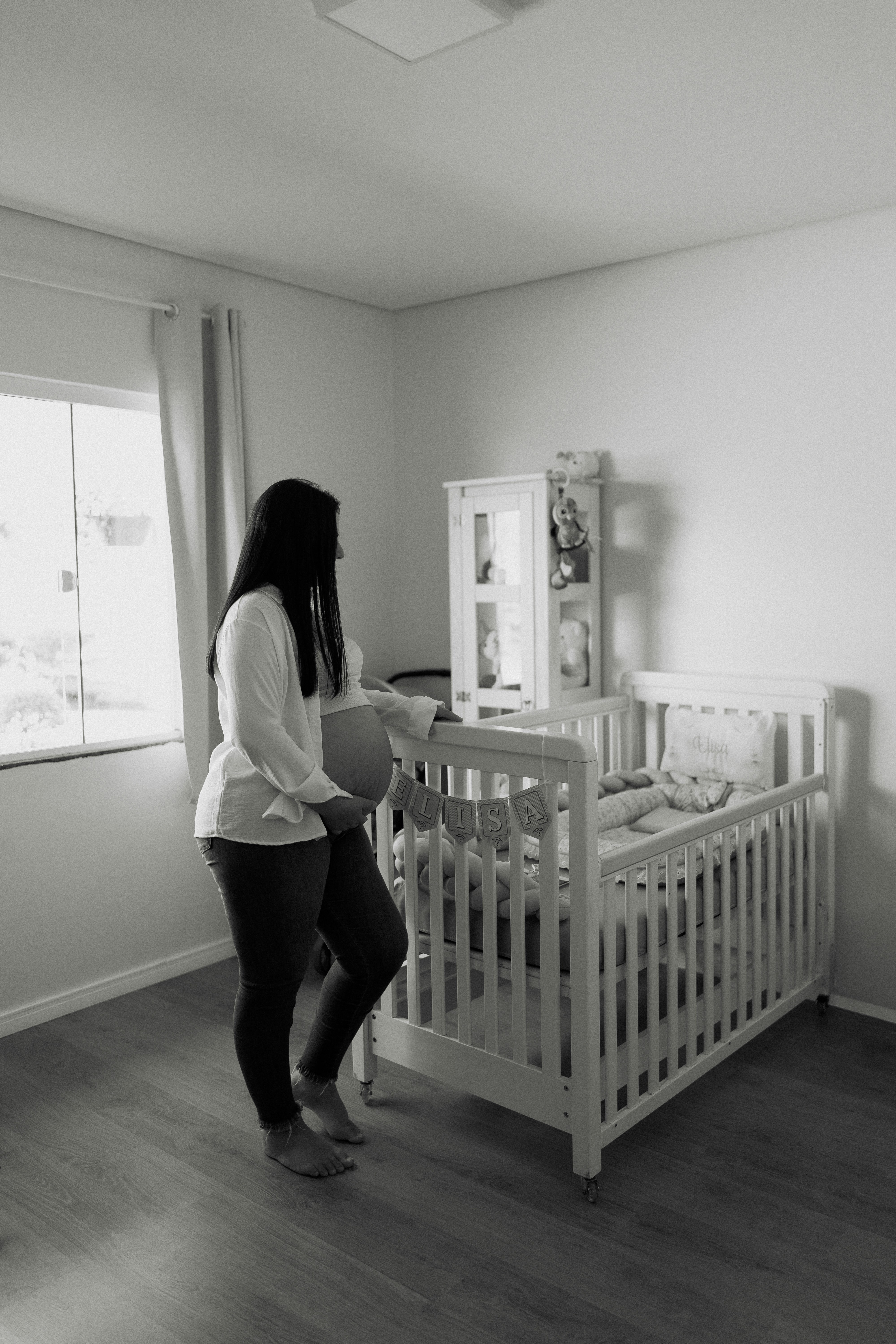 Pregnant woman looking at a crib in a nursery.