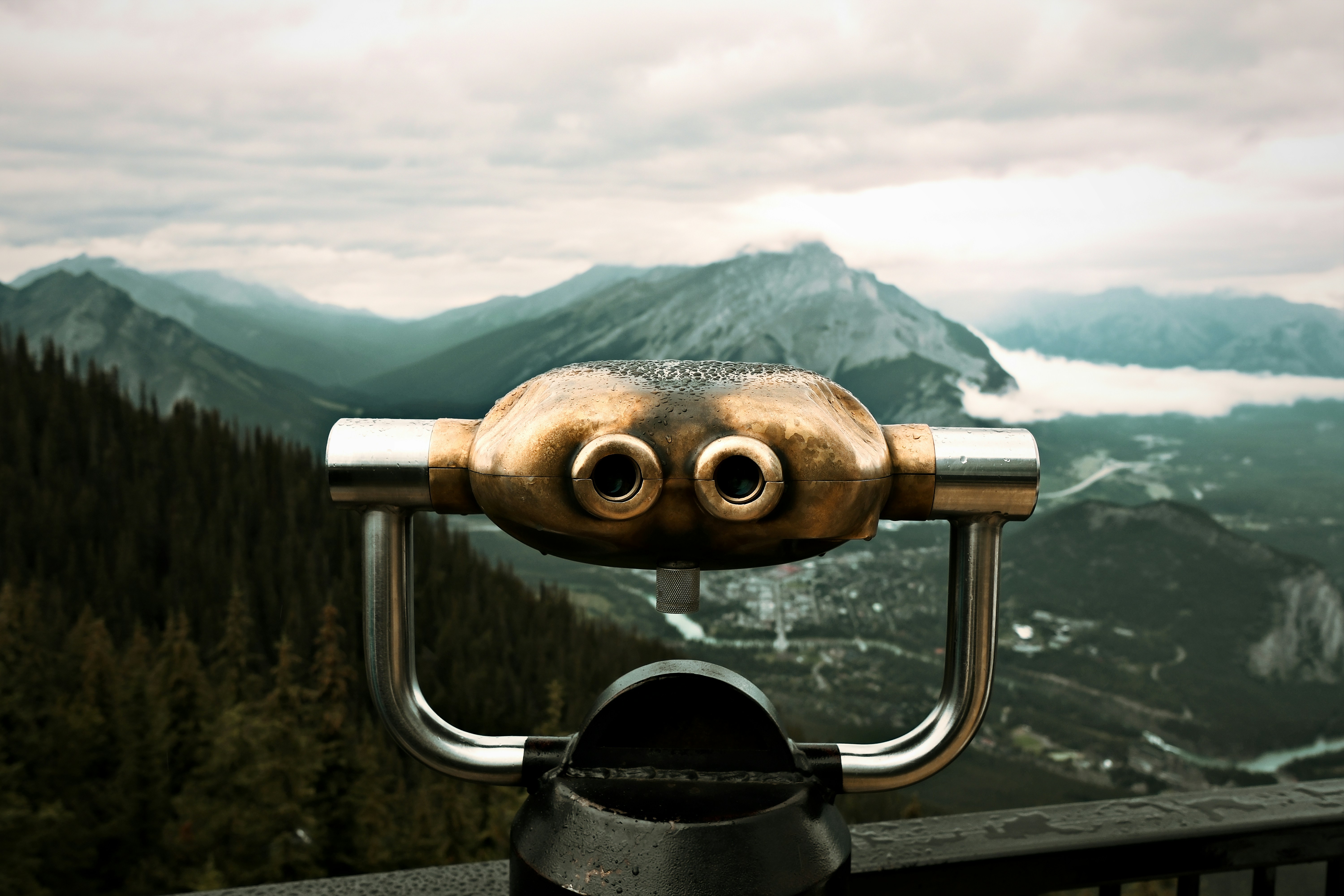 Binoculars overlook a misty mountain range and forest.