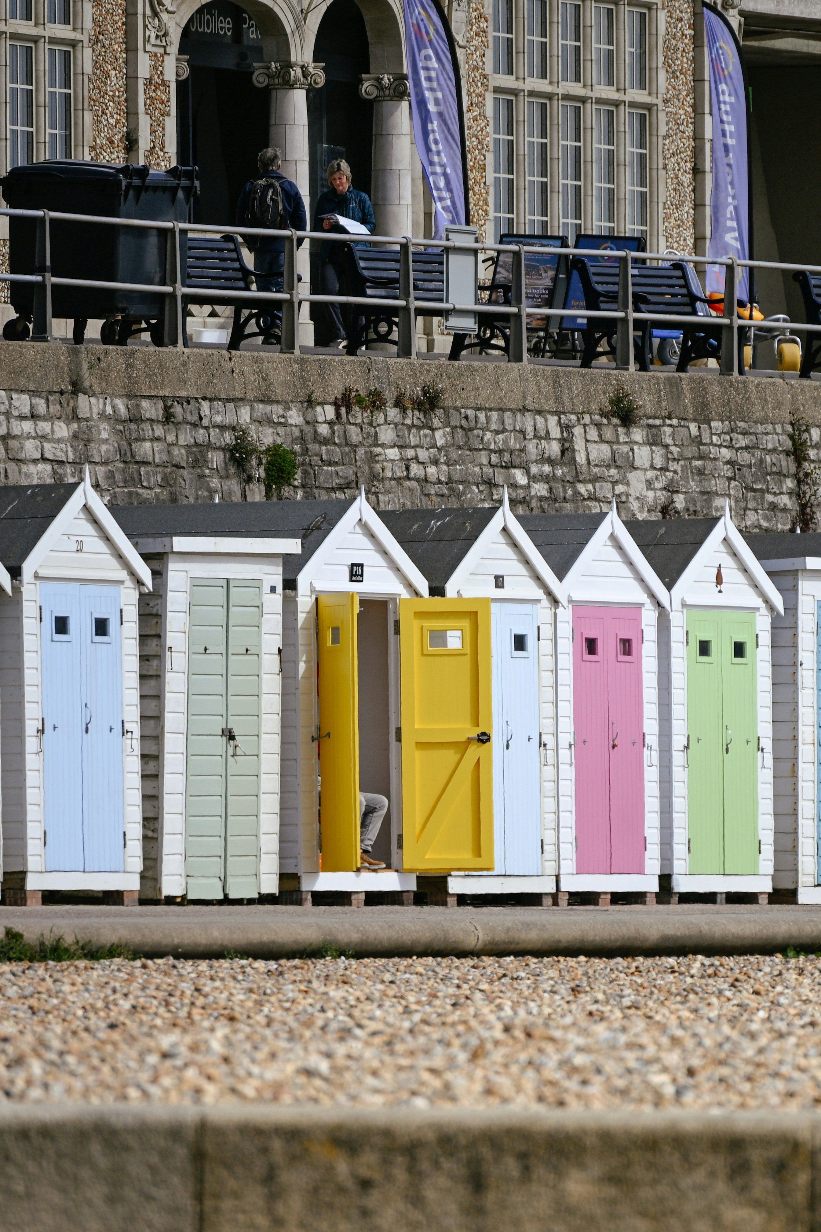 Colorful beach huts lined up on a pebble shore.