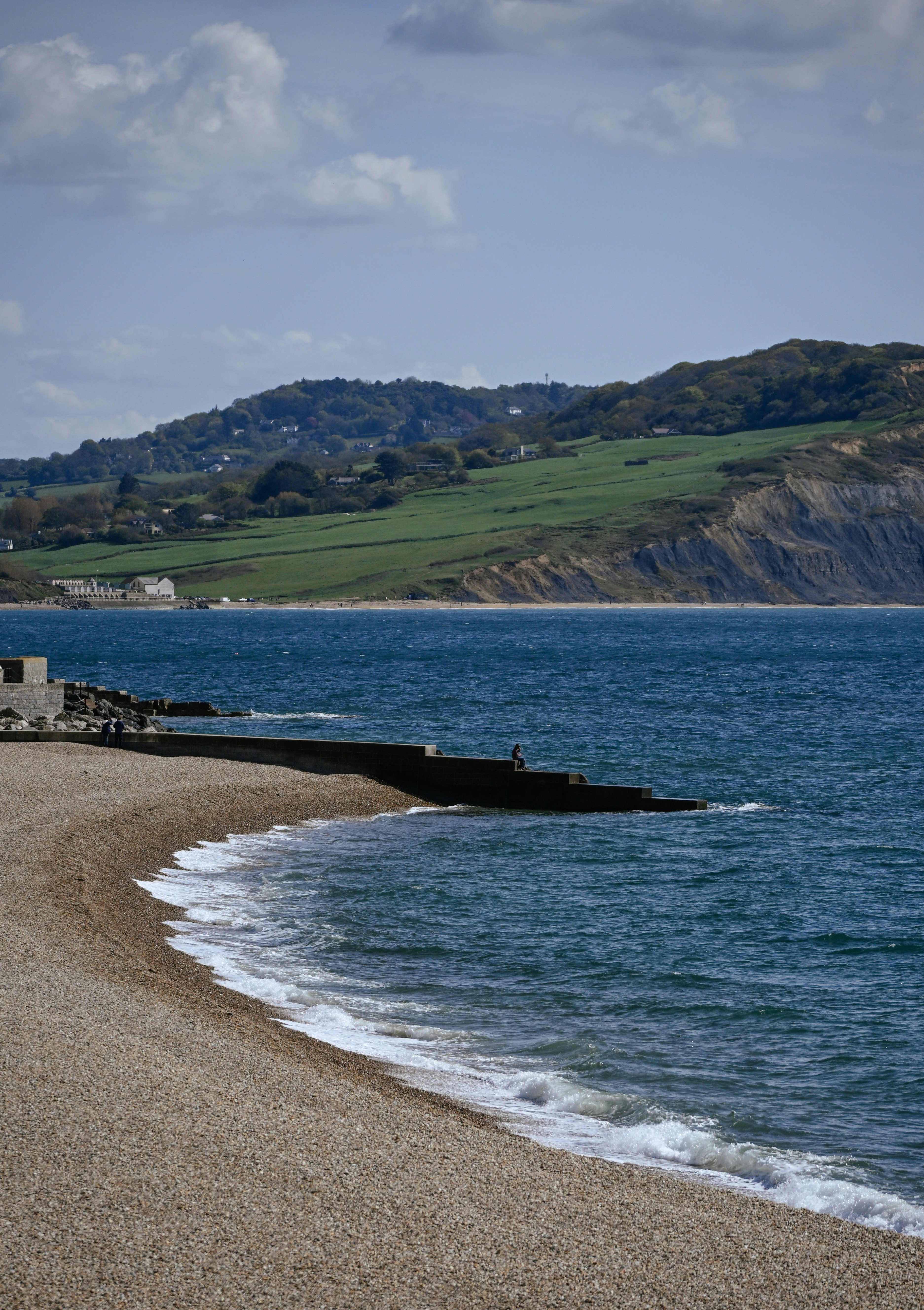 Pebble beach with waves and green hills.