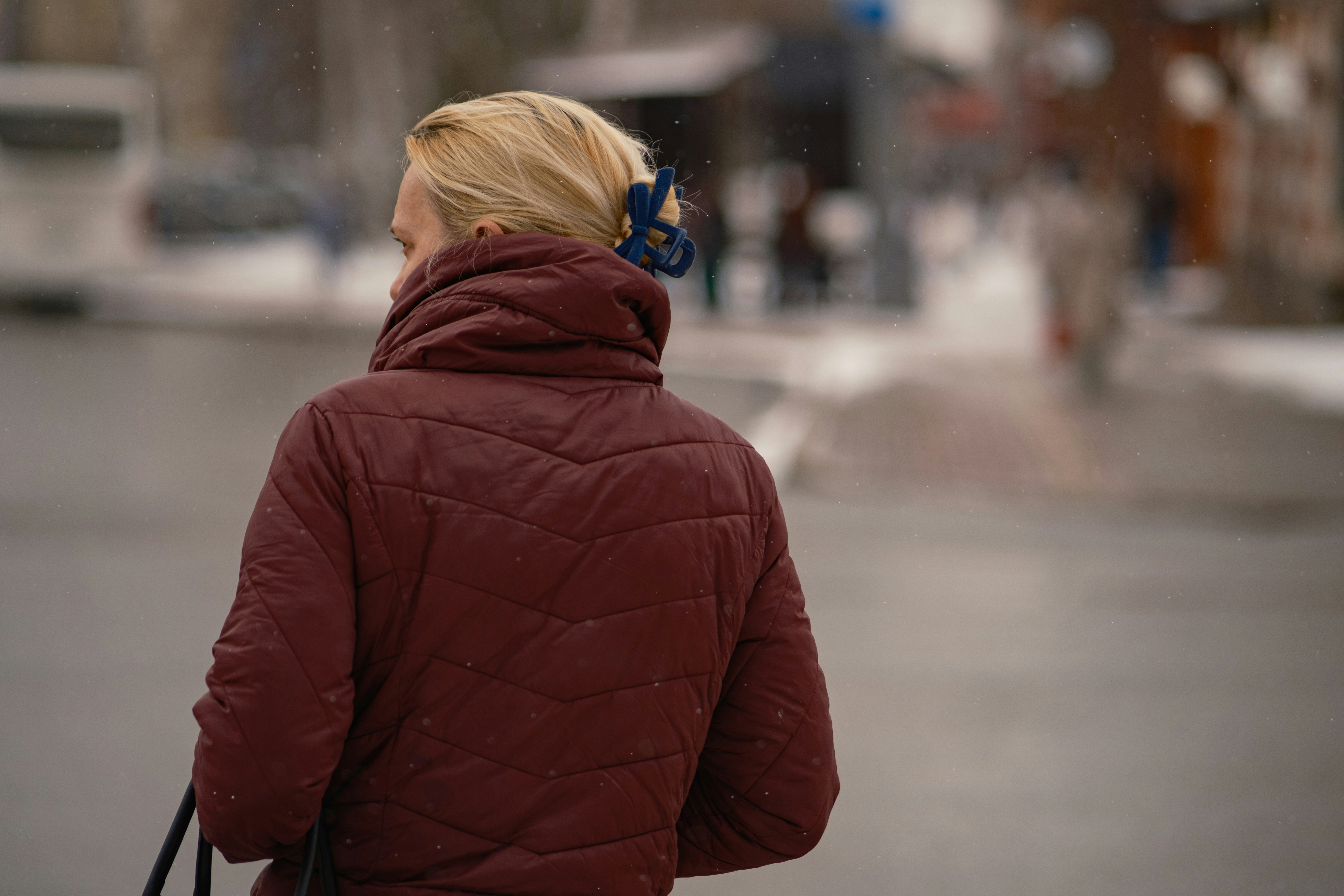 Woman in a maroon puffer jacket walking outdoors.