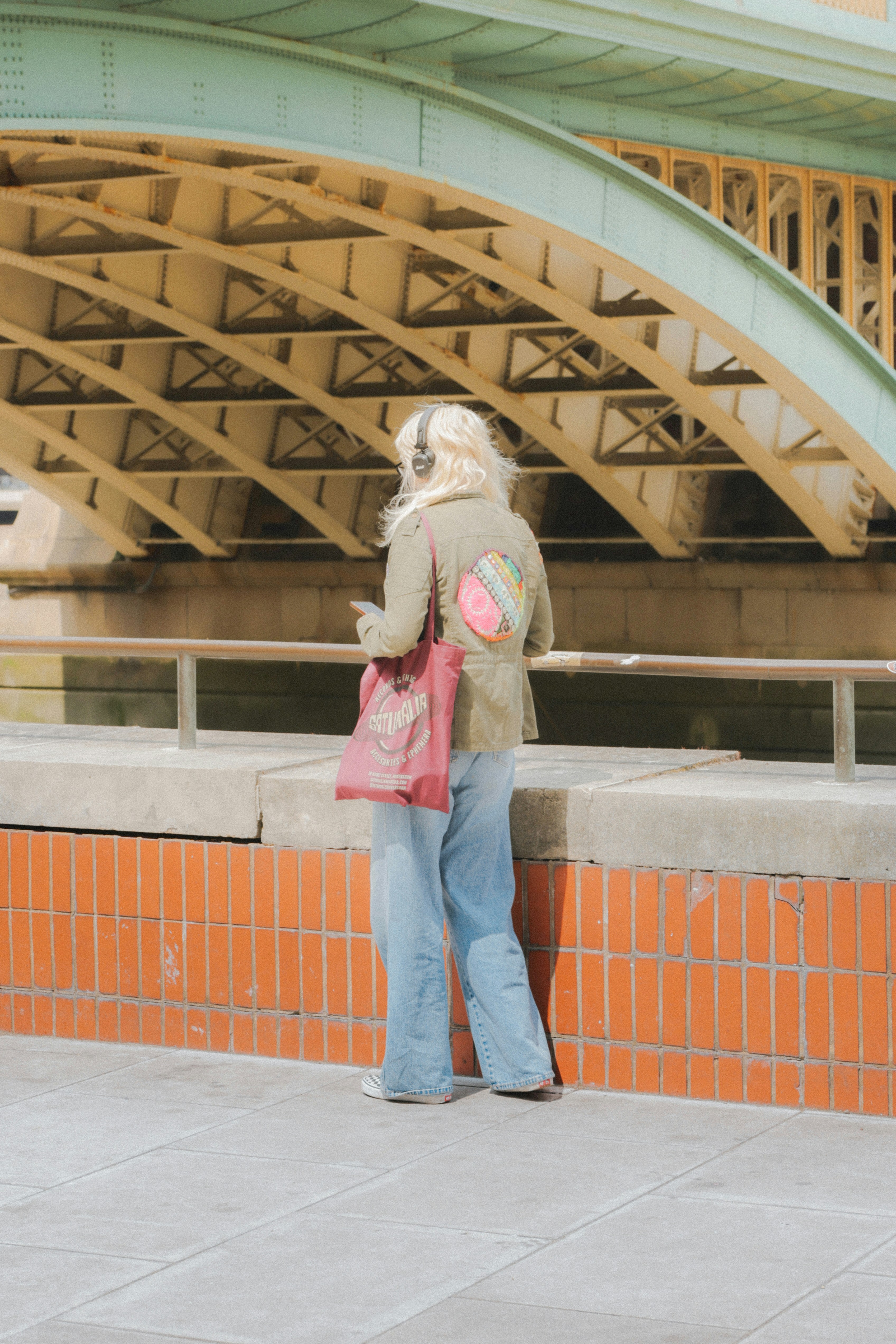 Woman with headphones and tote bag under bridge