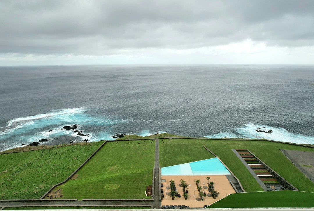 Ocean waves crash against a grassy cliff near a pool.