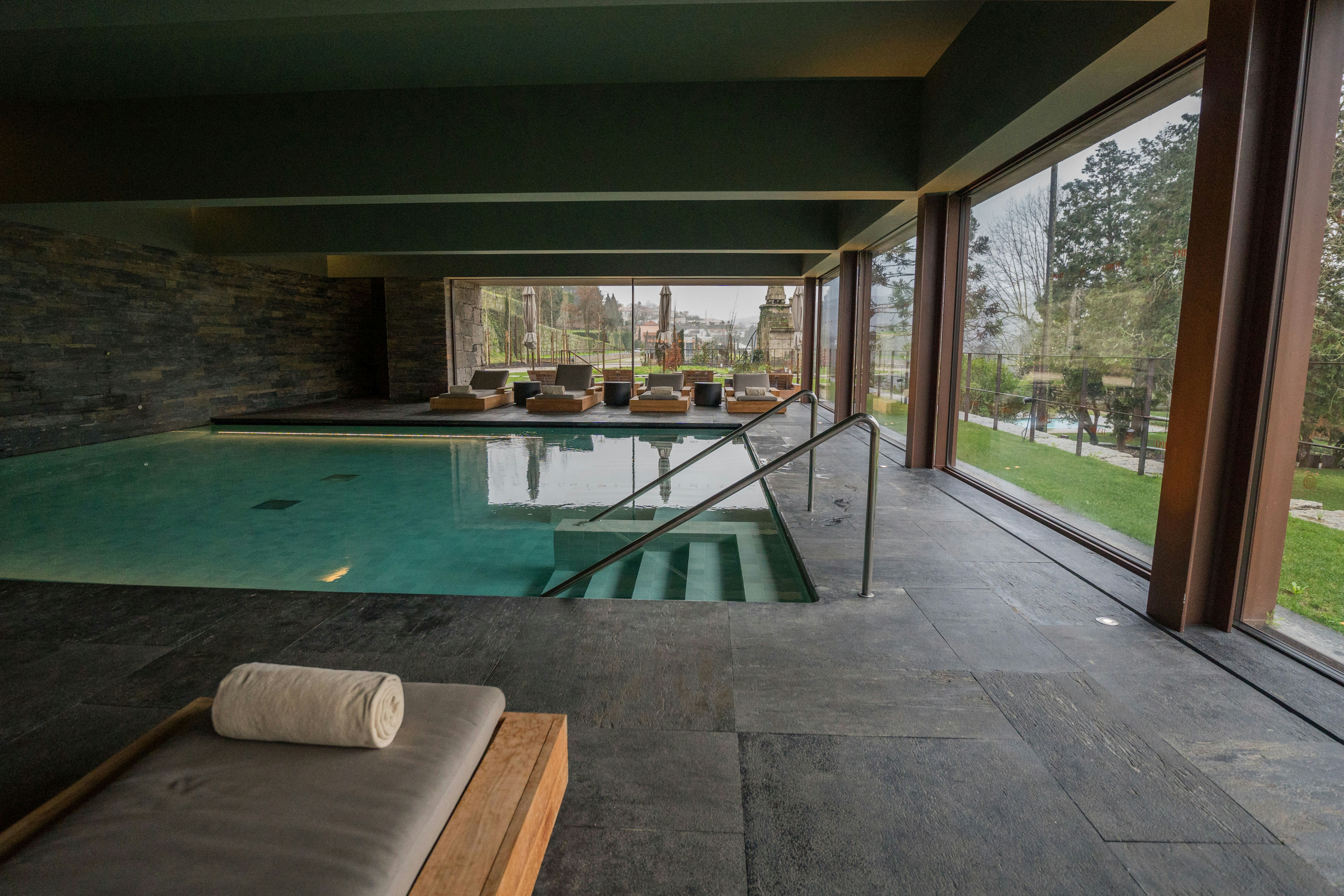 Indoor swimming pool with lounge chairs and large windows.
