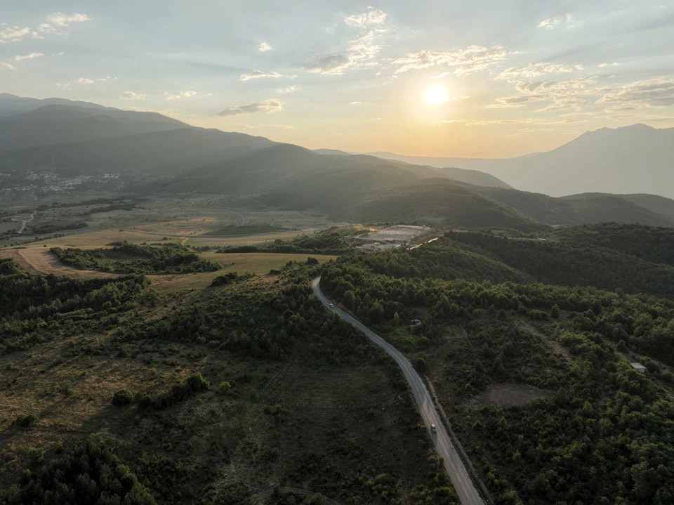 Winding road cuts through lush valley between two majestic mountains at sunset
