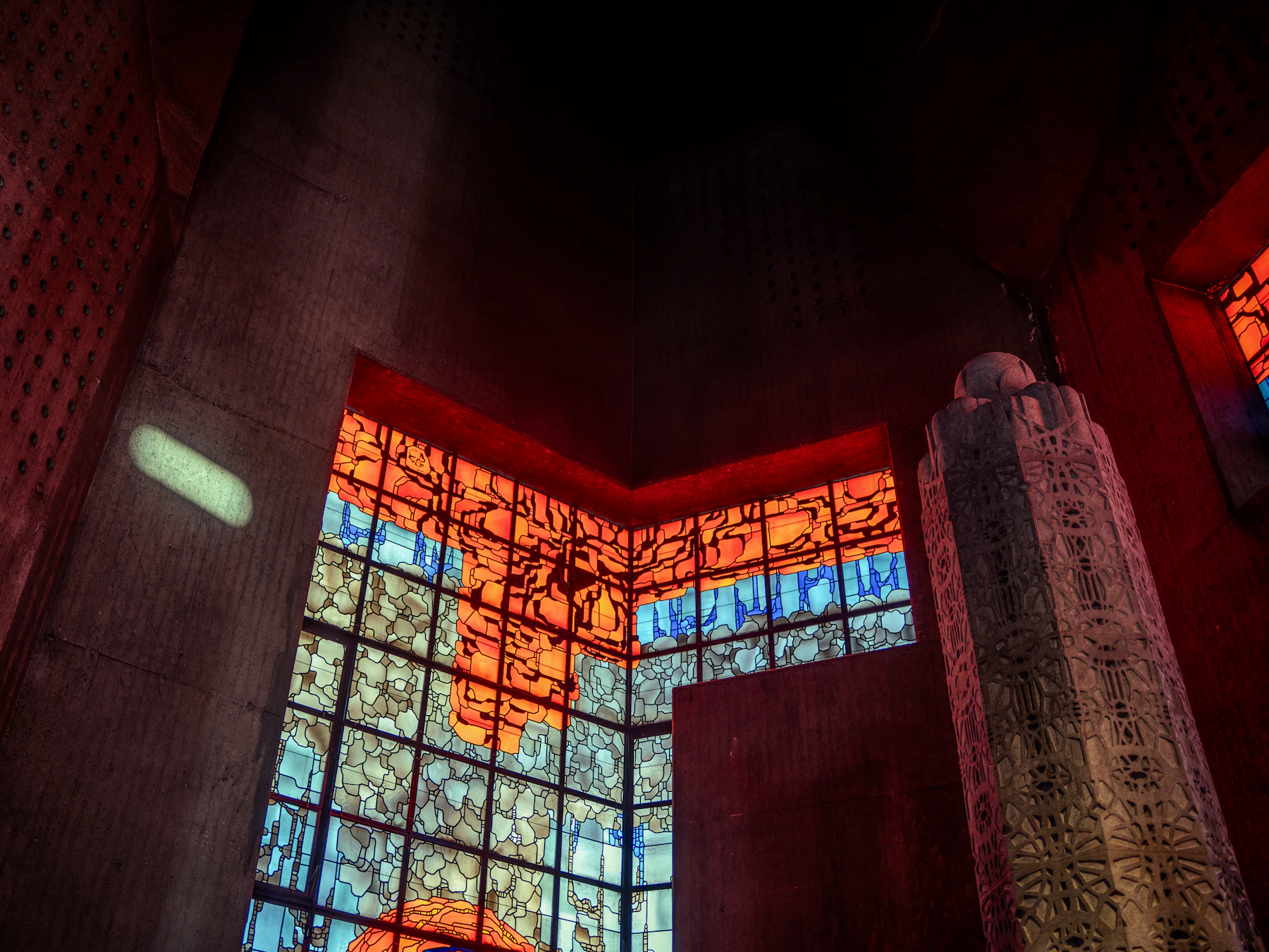 A stained-glass window in reds and blues throwing colour onto a stone wall