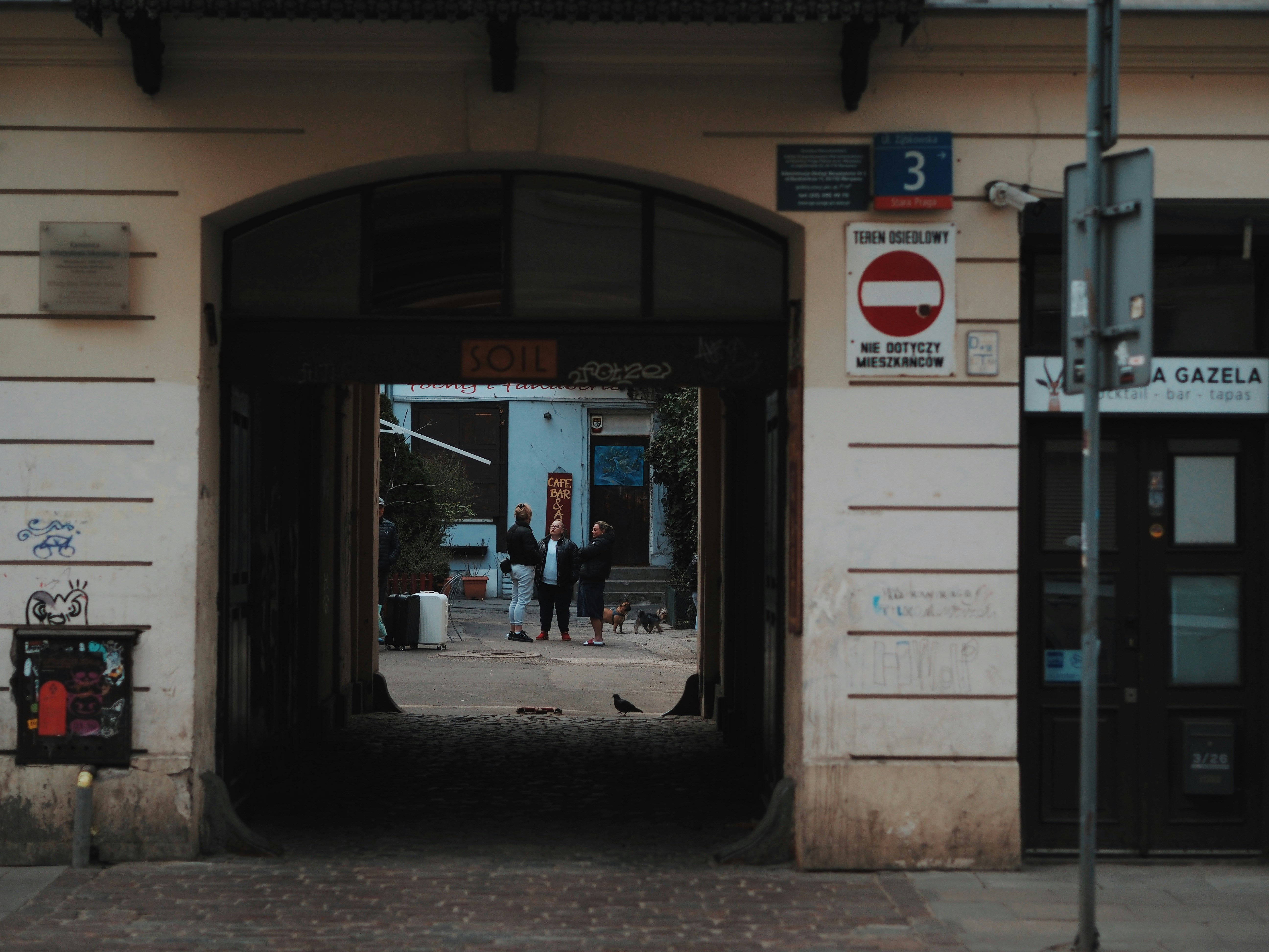 People walk through a dark archway into a courtyard.
