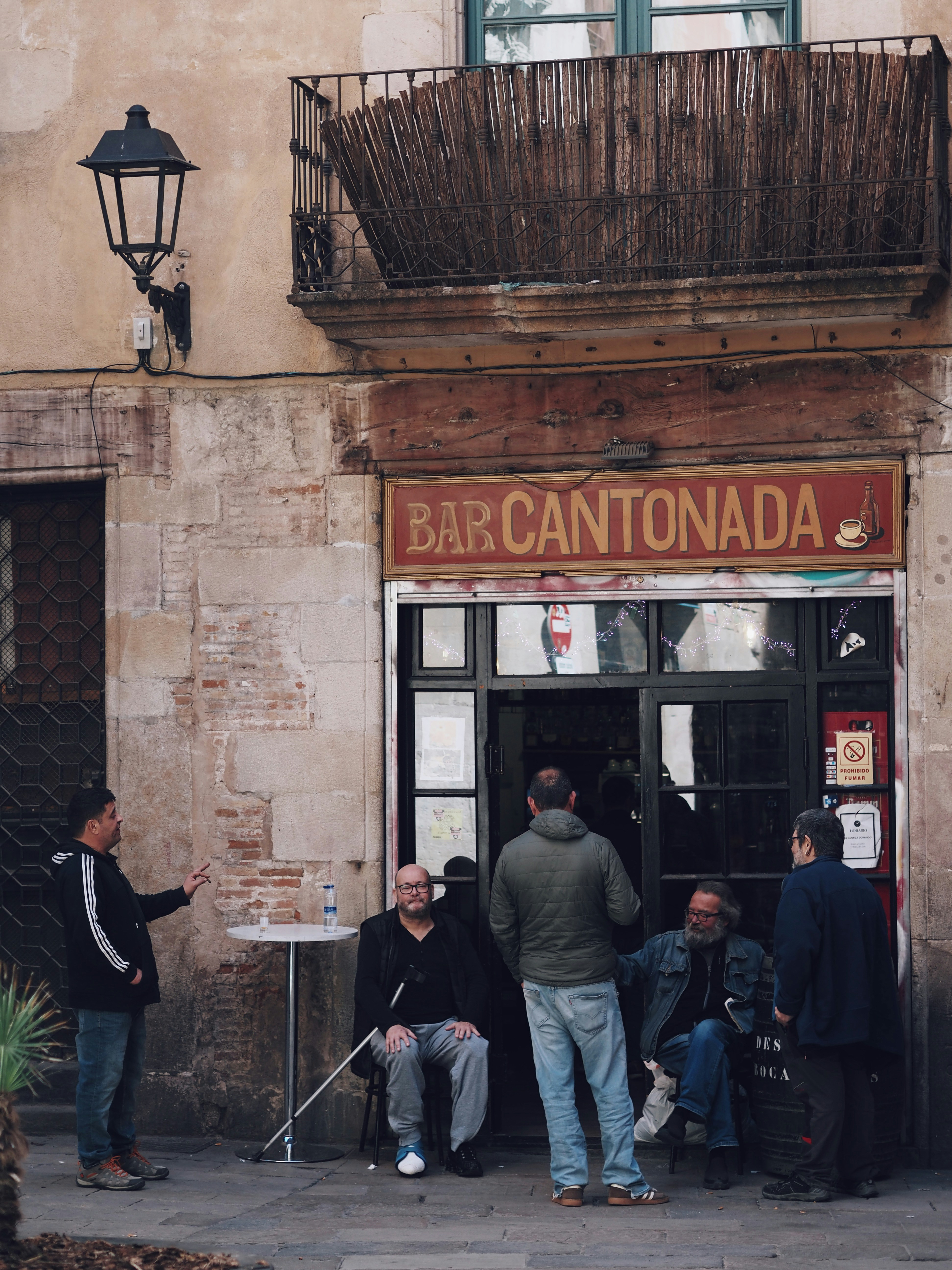 Men gathered outside a bar called bar cantonada.