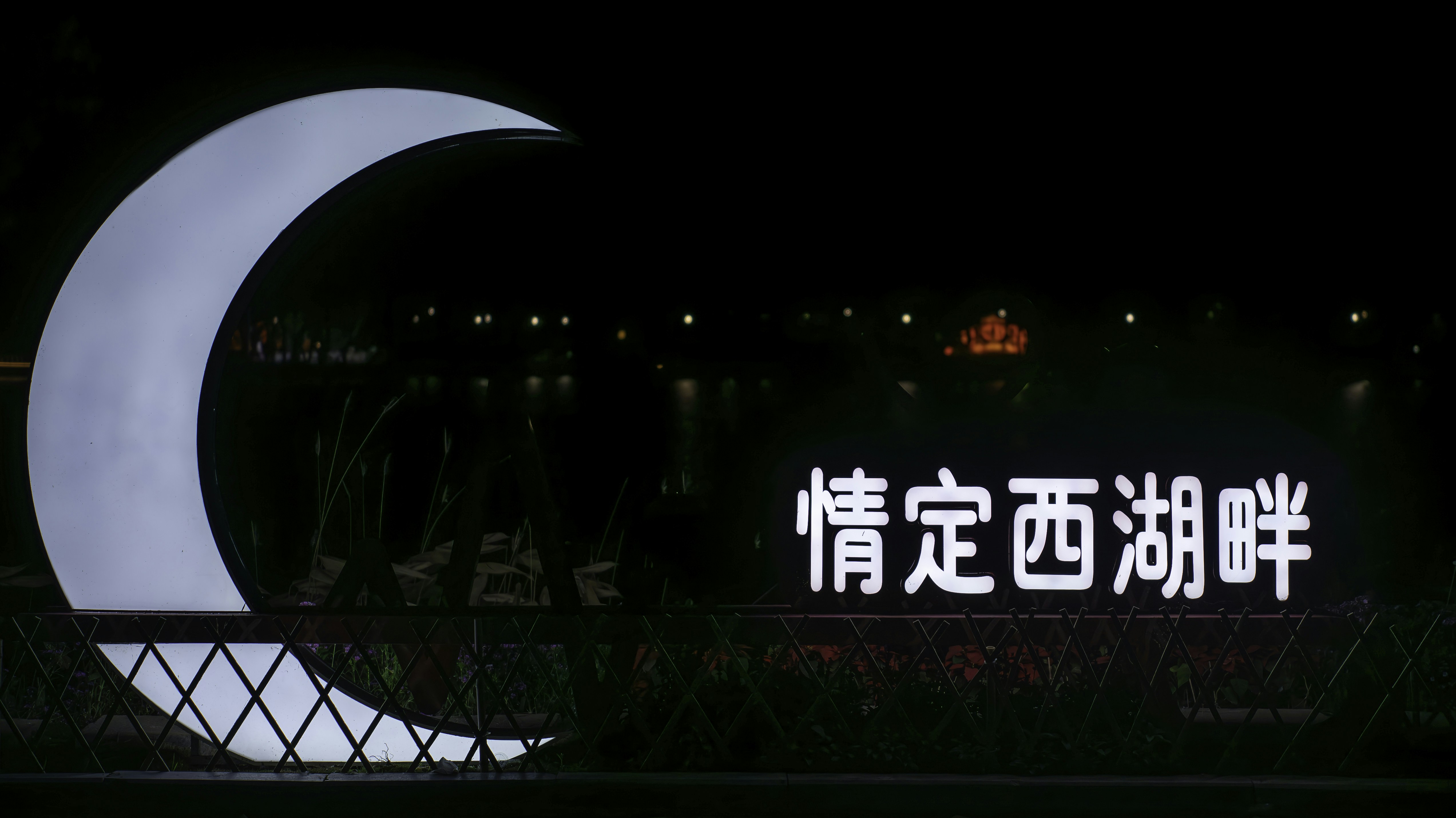 Large crescent moon sculpture at night with chinese text