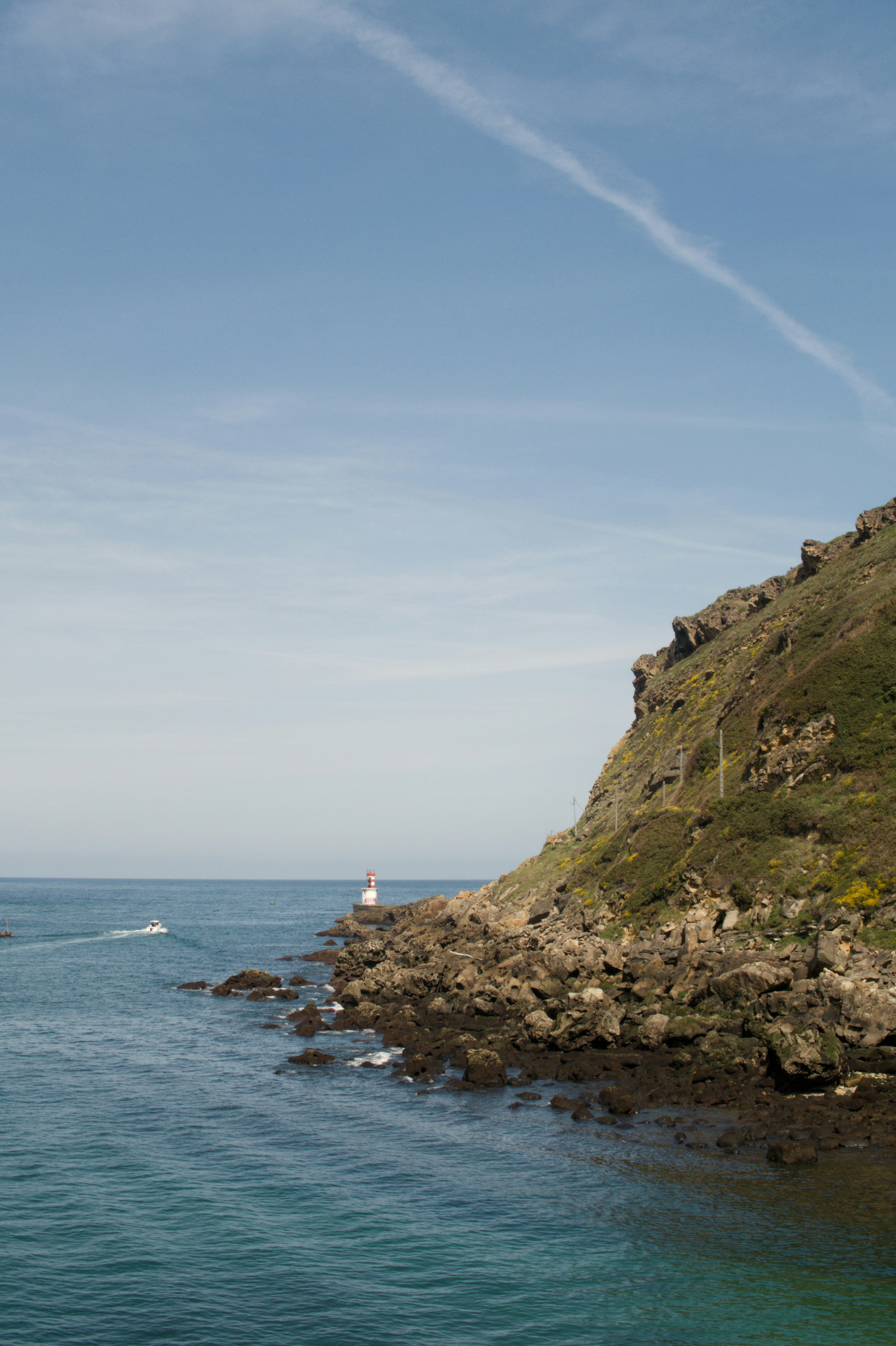Lighthouse on rocky coast with boat in the ocean