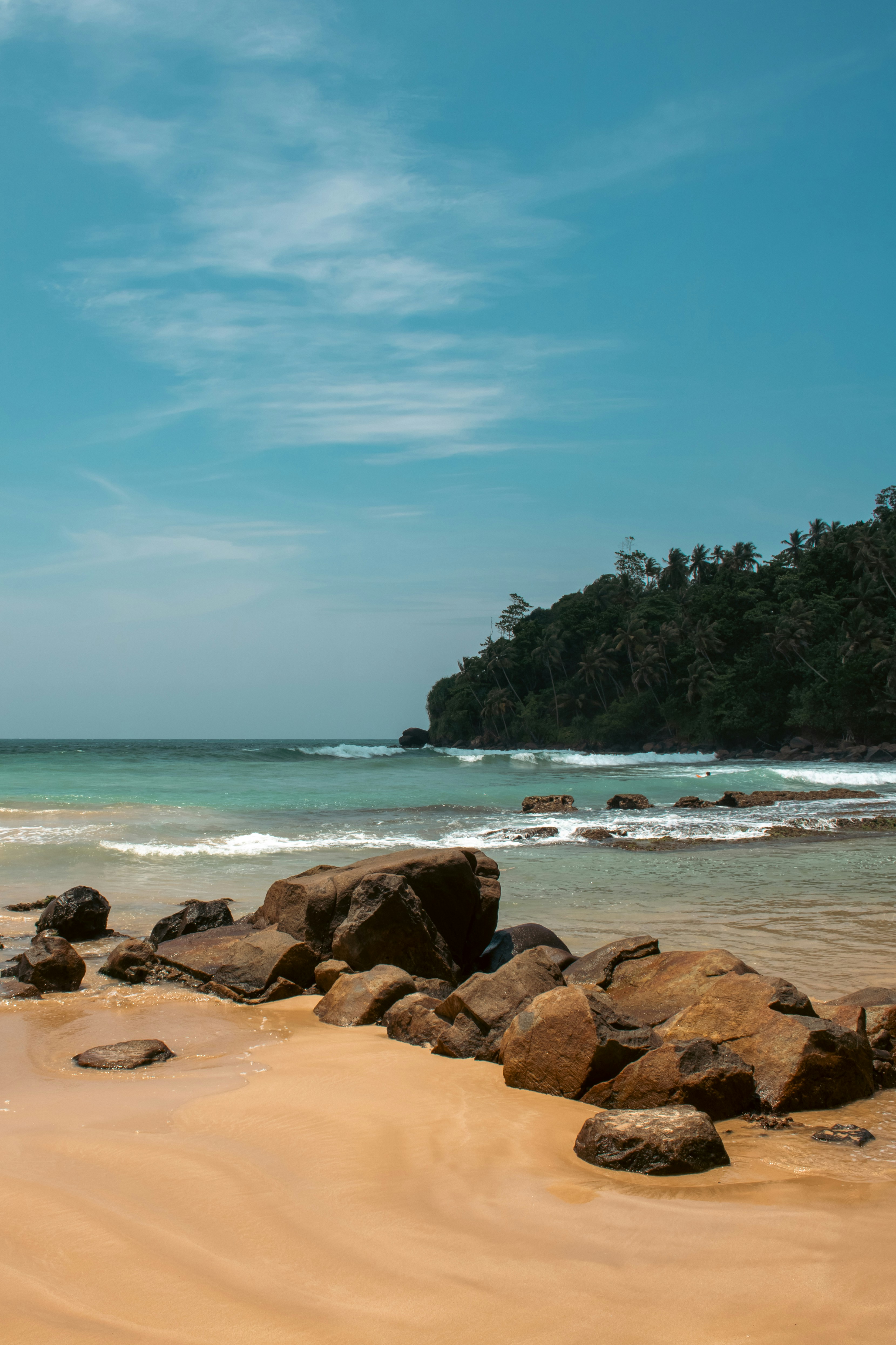 Rocky beach with turquoise water and lush green hills.