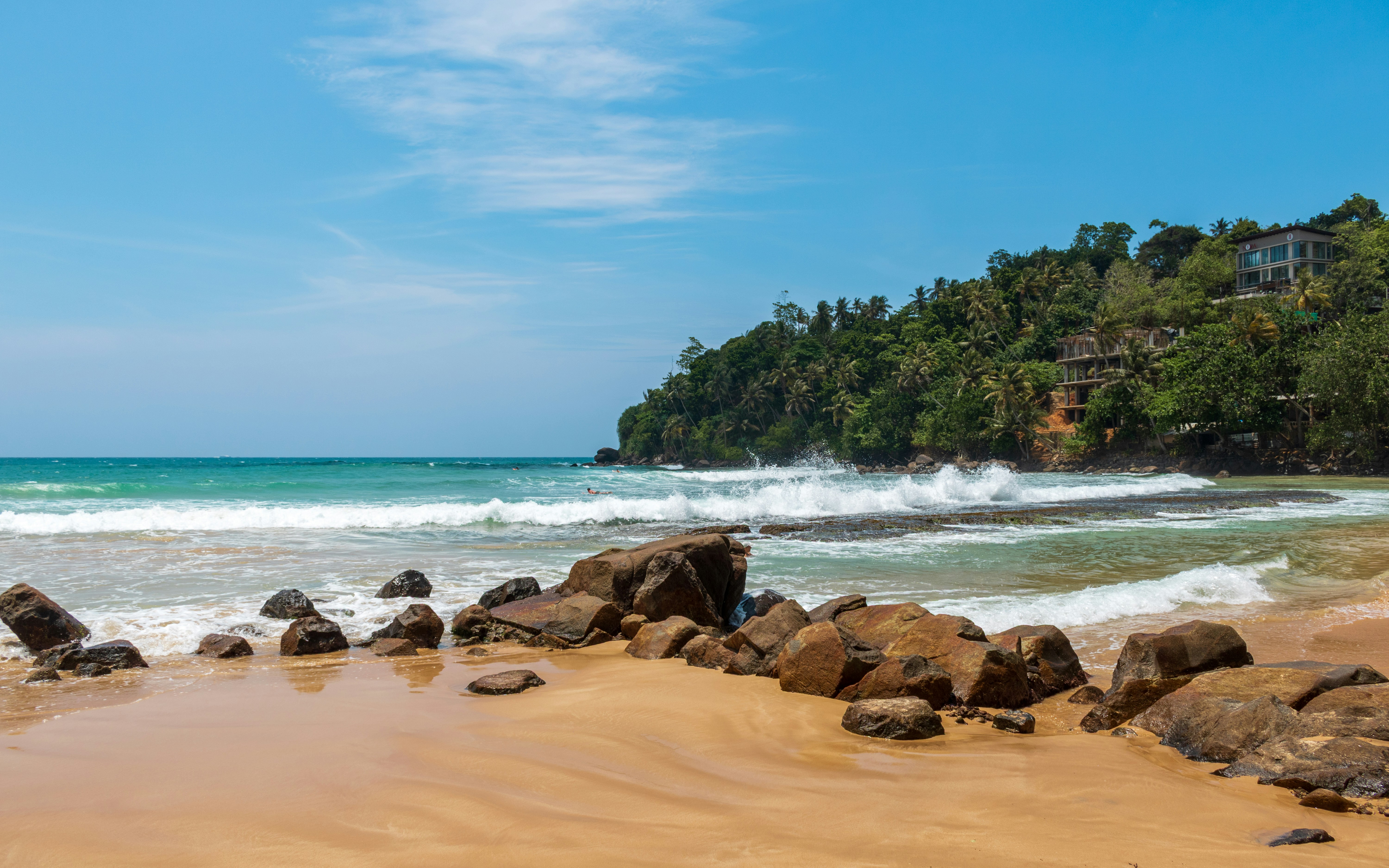 Waves crashing on a rocky beach with lush green hills.