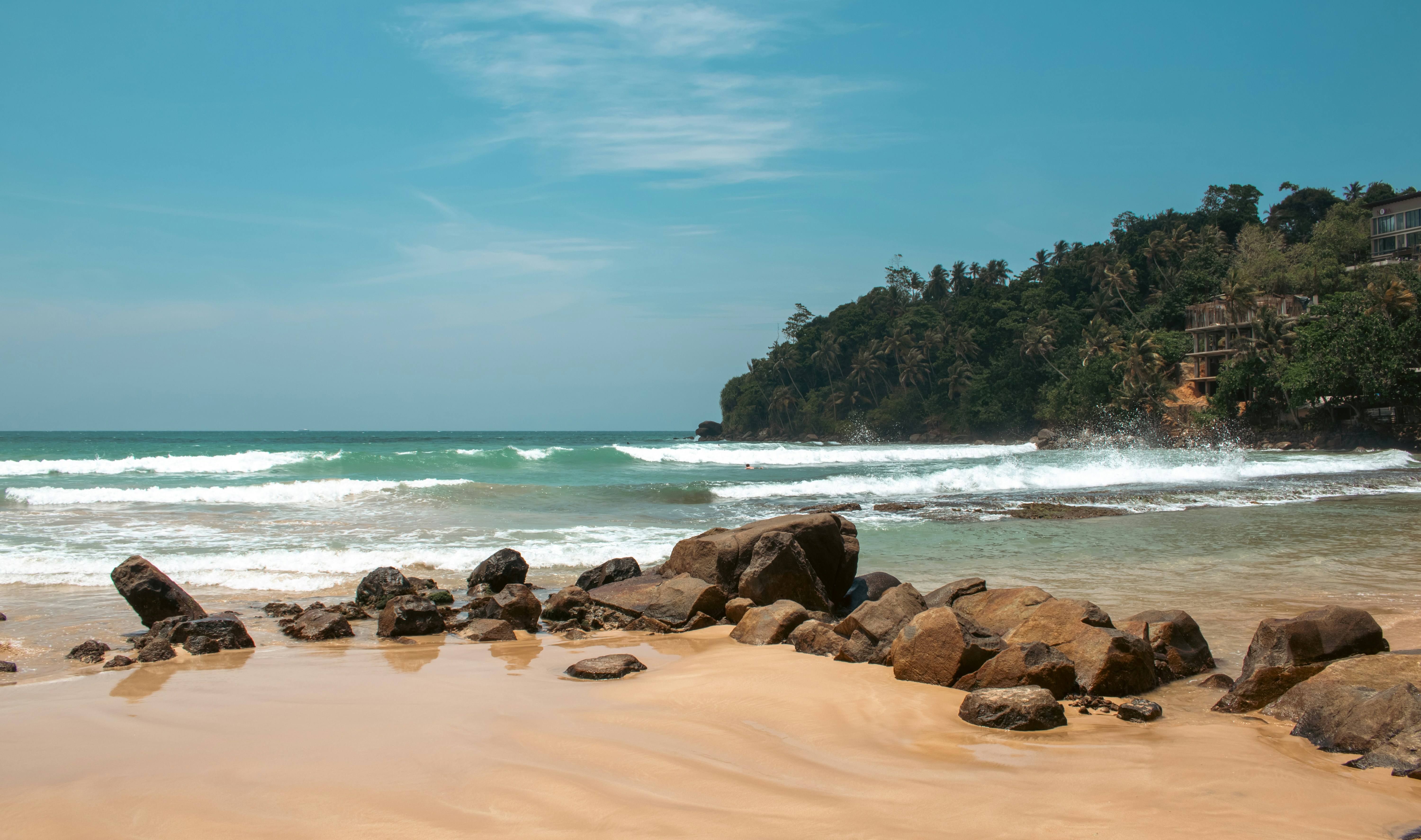 Waves crashing on a rocky beach with lush green hills.