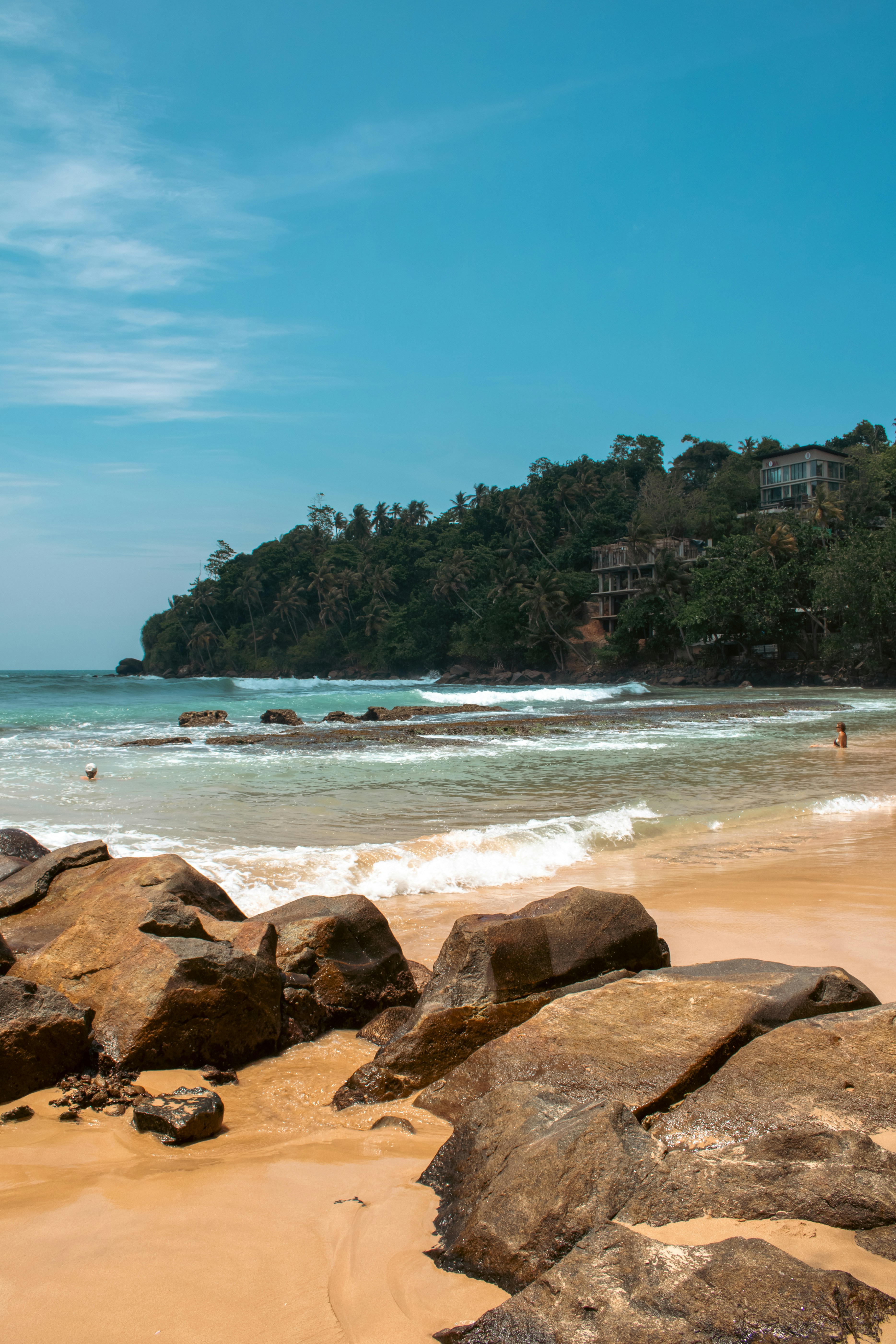 Rocky beach with waves and lush green hillside.