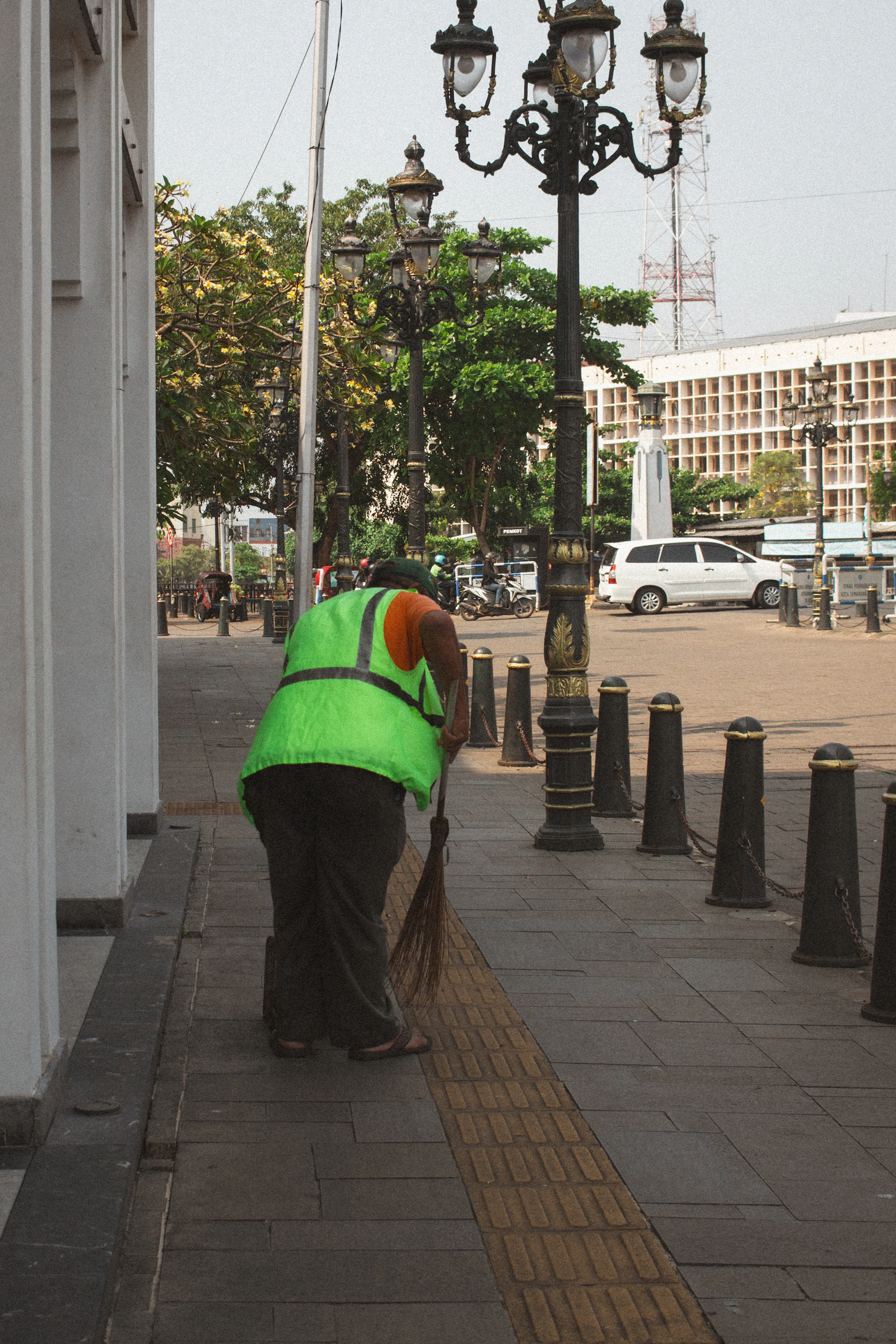 A street cleaner sweeps a sidewalk with a broom.